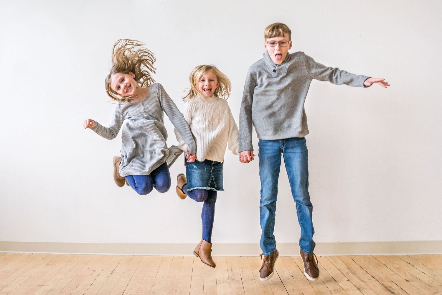 A family jumping and playing together against a white wall in casual attire.