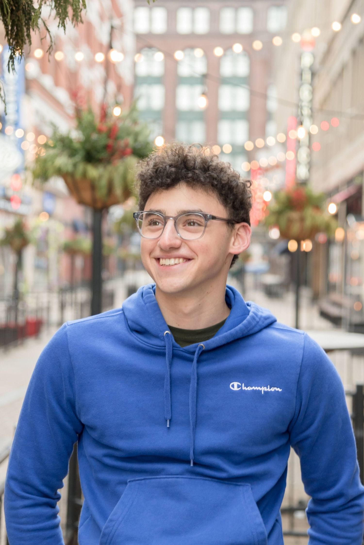 Casual portrait in blue Champion hoodie under festive string lights and holiday decorations.
