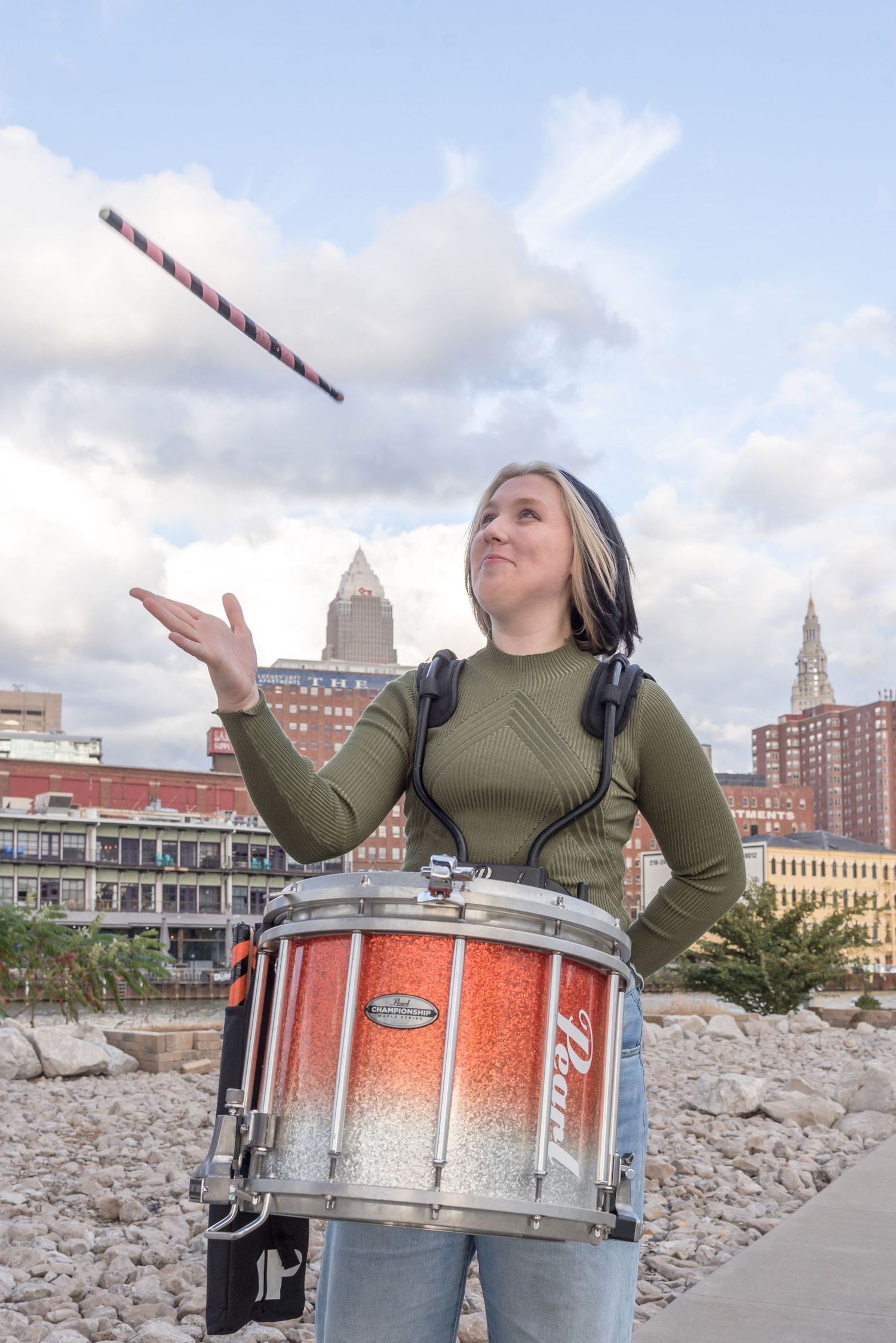 Drummer performing with orange drums against an urban skyline backdrop.
