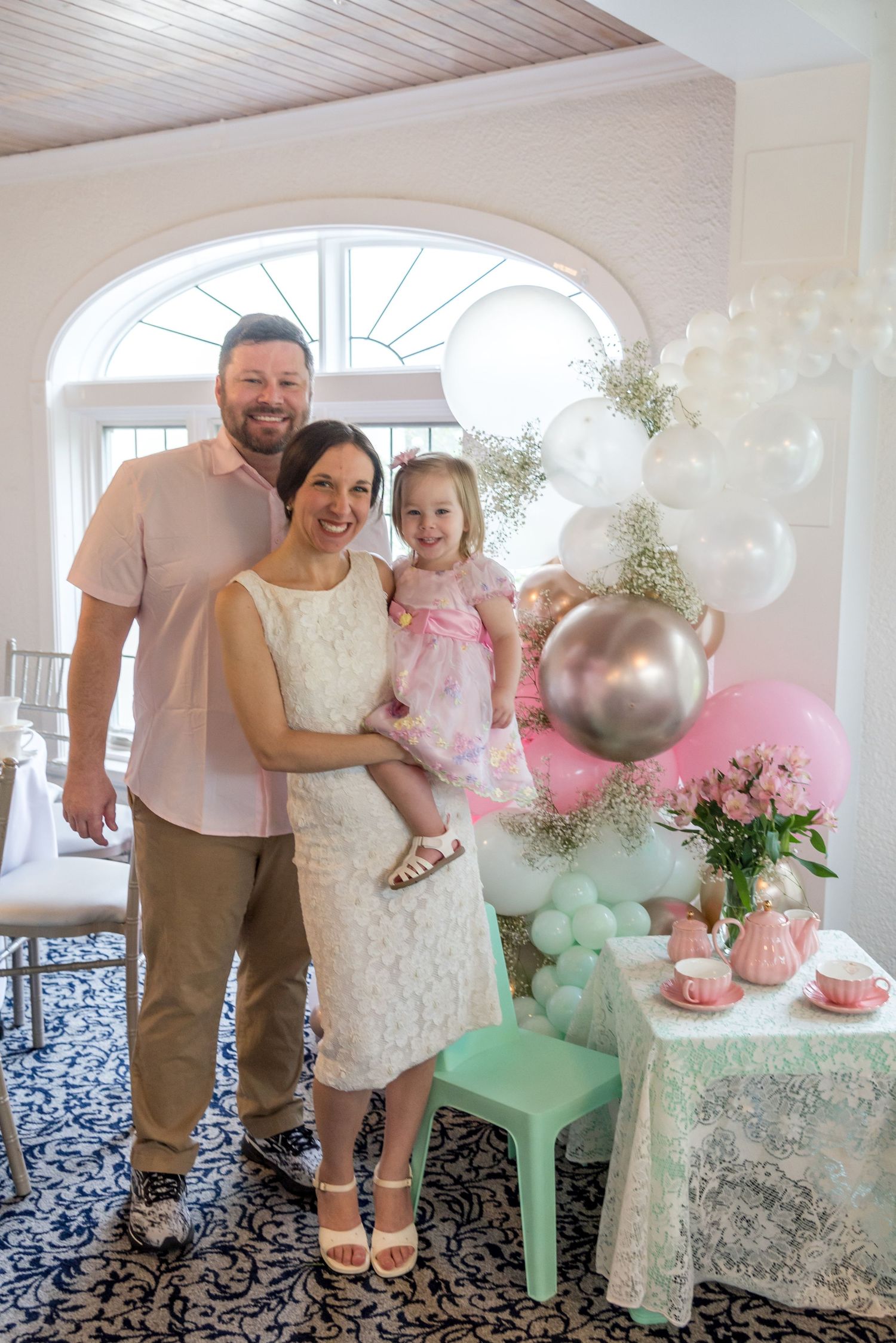 A celebratory scene with pink and mint balloons, floral arrangements, and a decorated tea party setting.