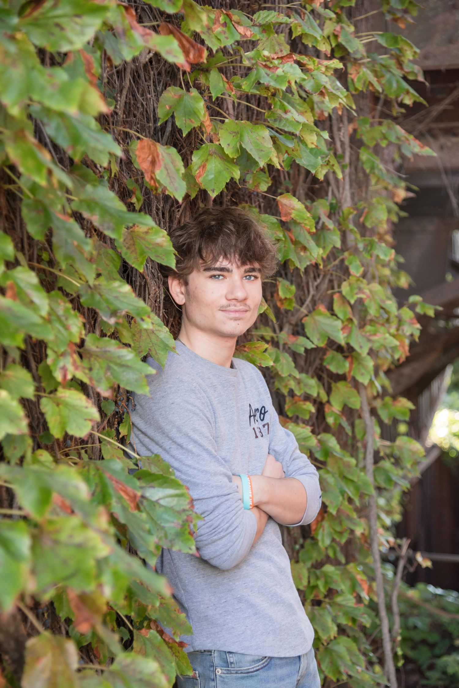 Student in grey sweatshirt poses against autumn vine-covered wall.