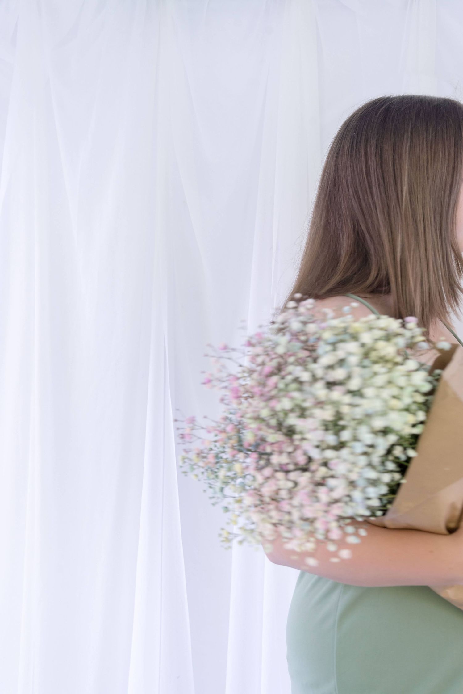 Person holding delicate baby's breath flowers against white curtain background.