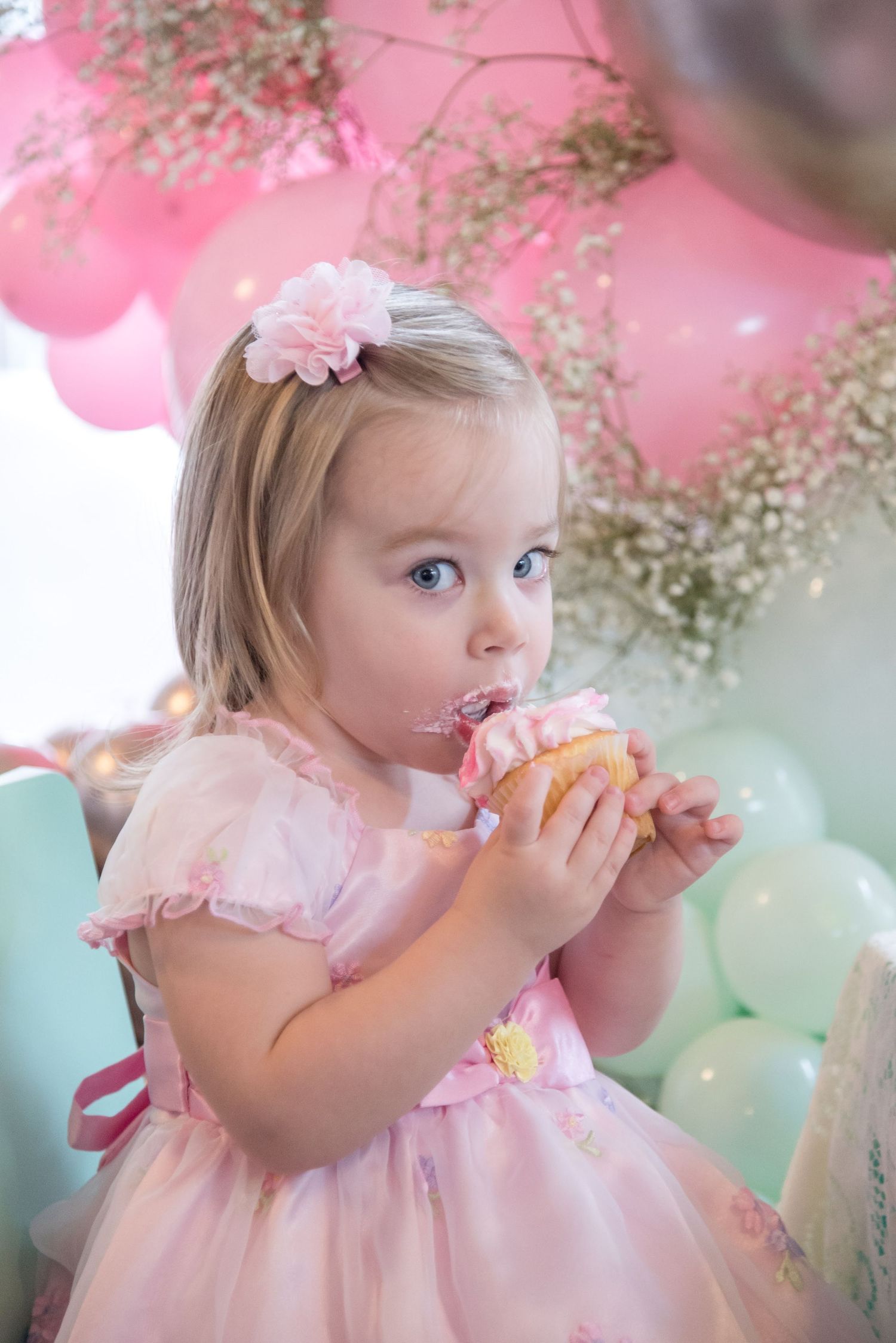 Young child in pink dress enjoying treats at a pastel-themed party.