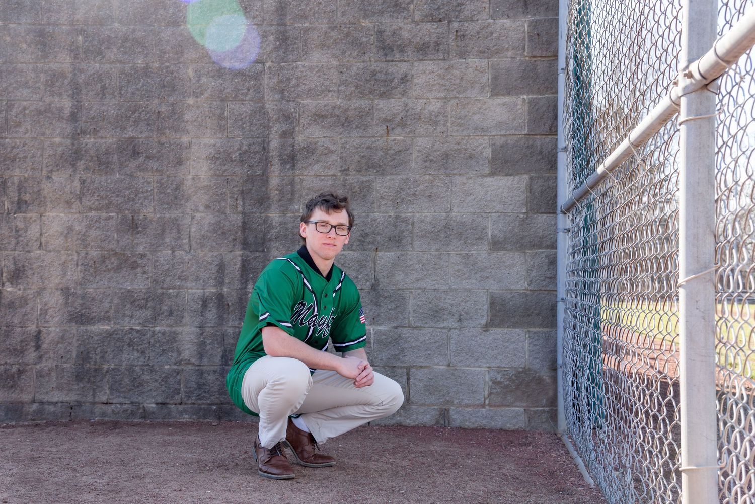 Portrait in green shirt against concrete wall in athletic dugout setting.