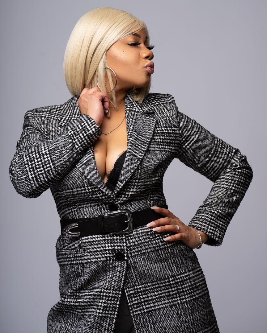 A model poses in a structured black and grey plaid blazer against a grey studio backdrop while showcasing different angles.