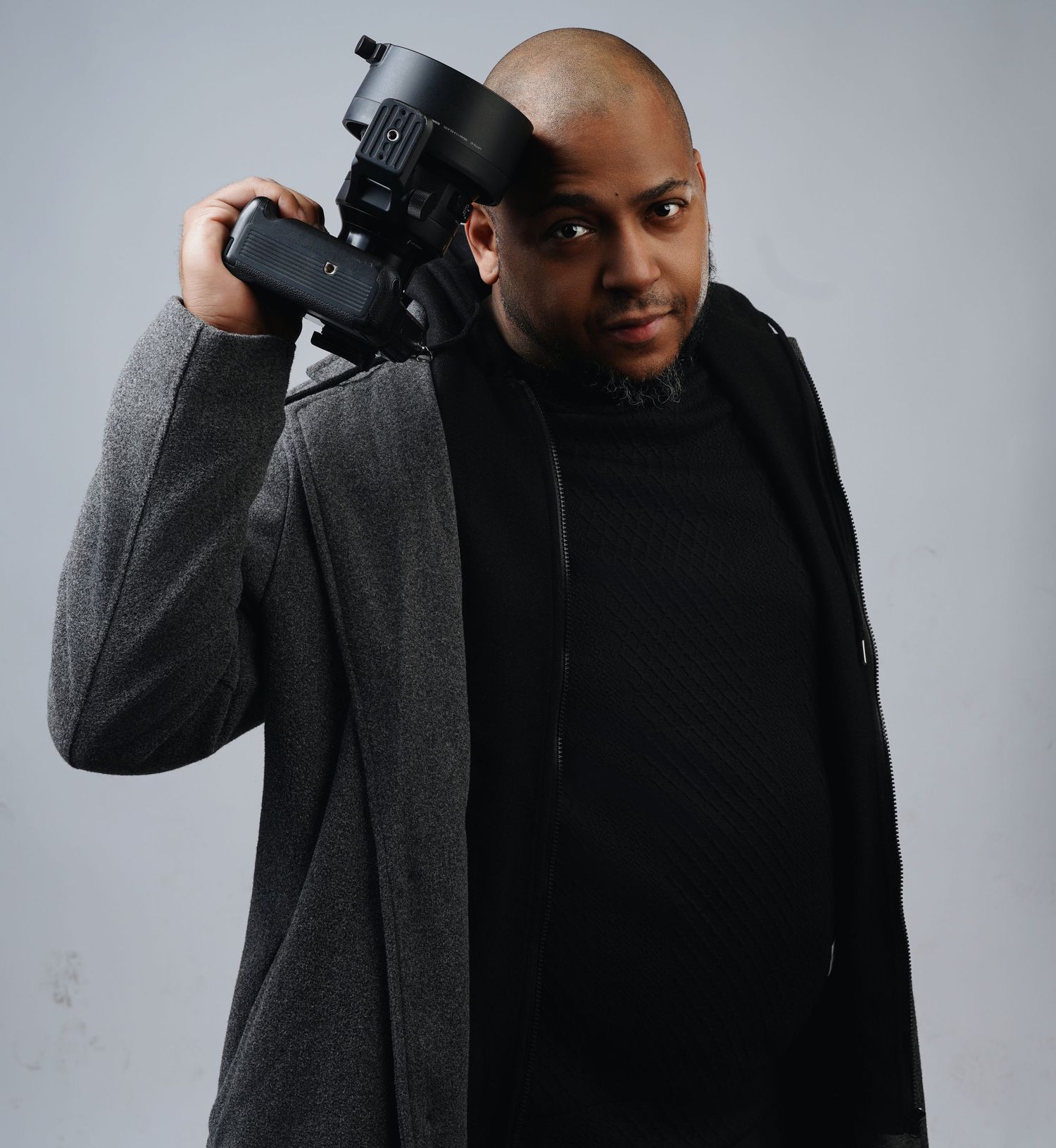 Creative portraits with camera equipment wearing grey coat against light background.