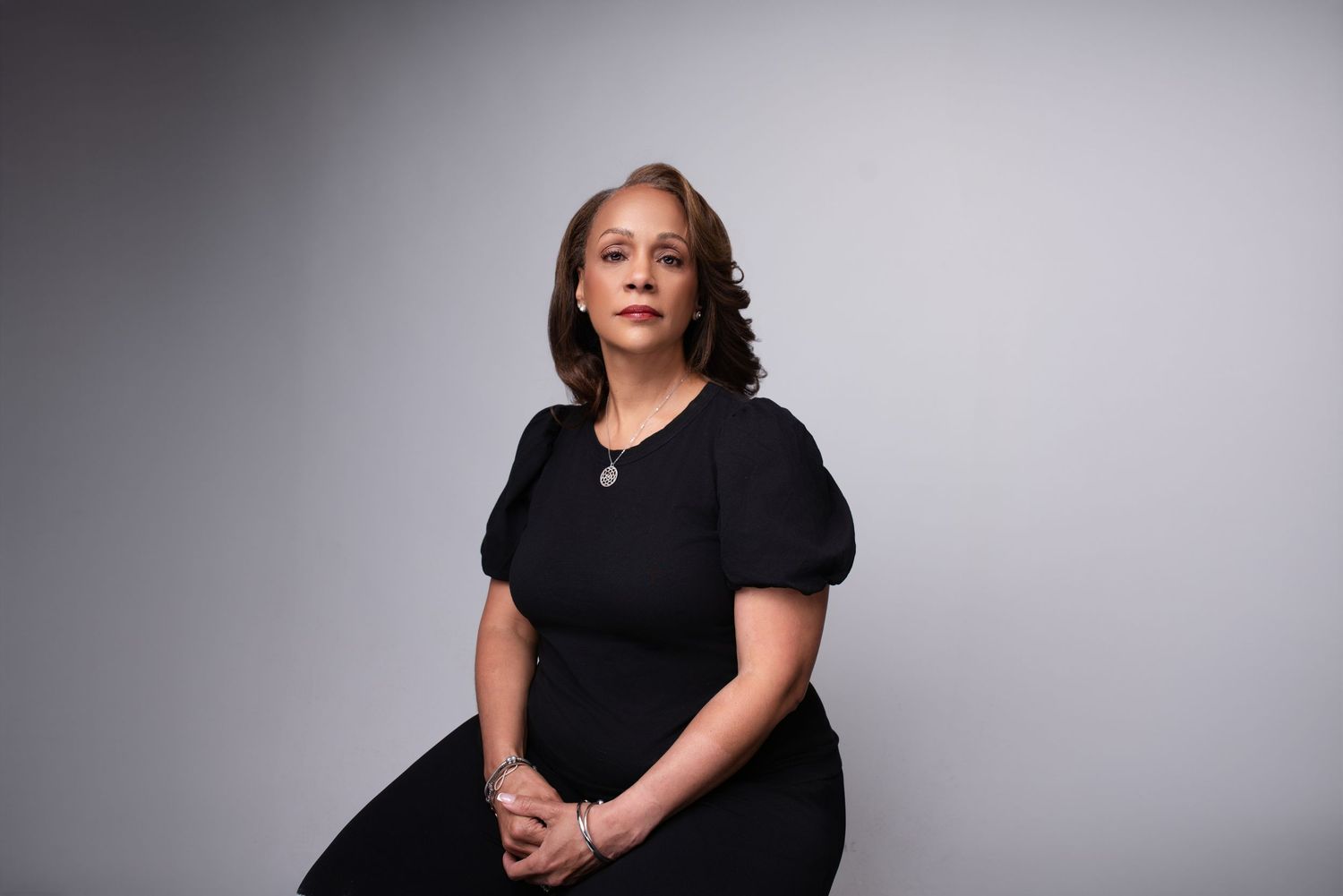 Studio portrait of person in black dress against gray background with contemplative expression.