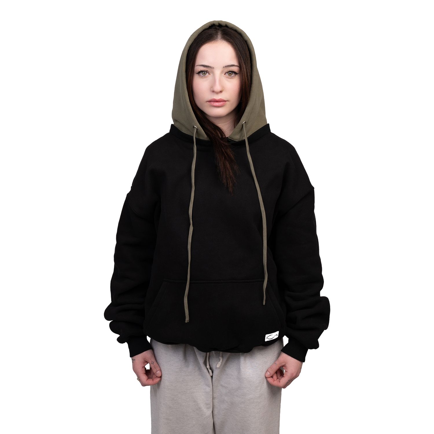 Person in black oversized hoodie with olive green hood and light gray sweatpants standing against white background.