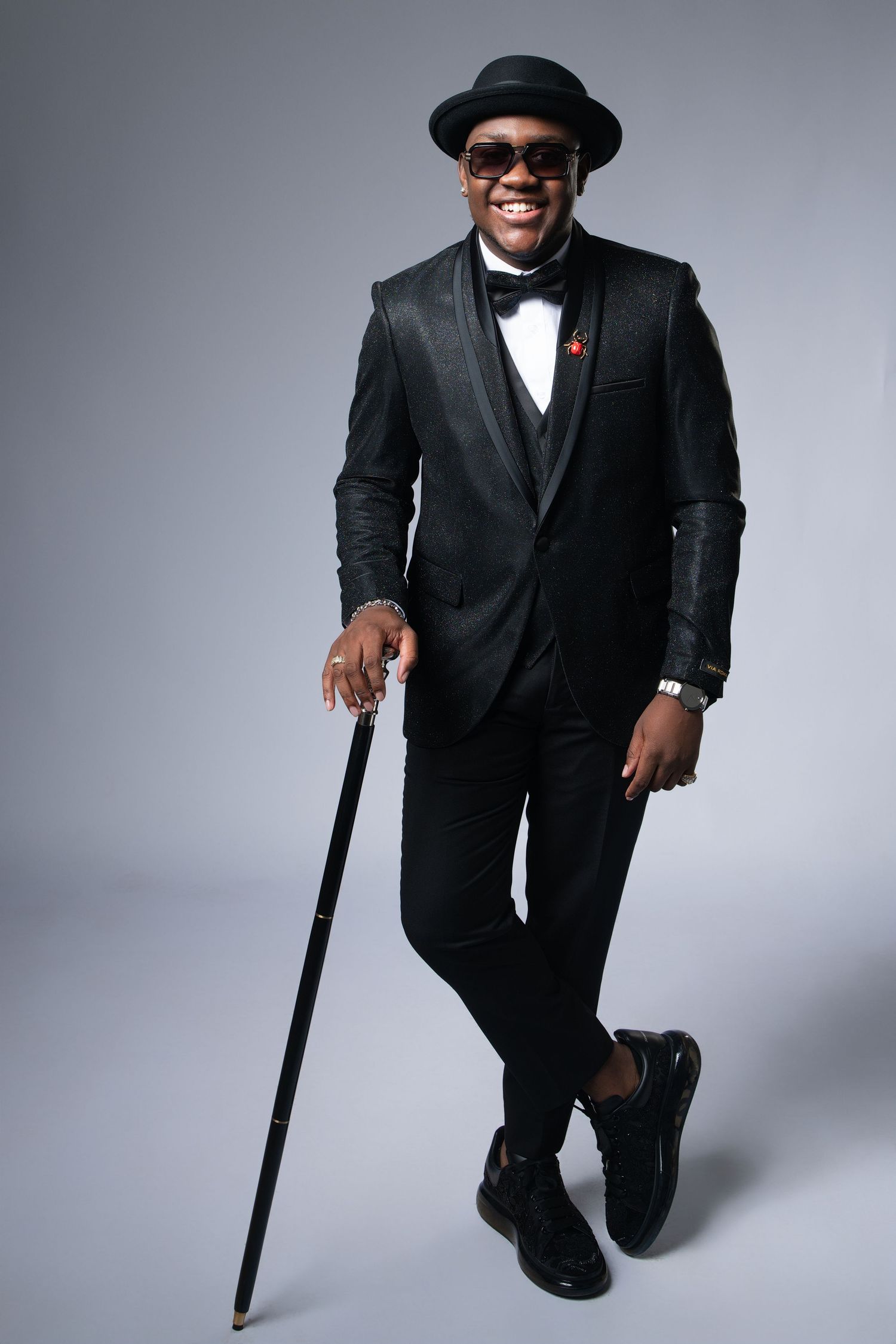 Dapper styling in black tuxedo, hat and bow tie with walking cane creating elegant pose.