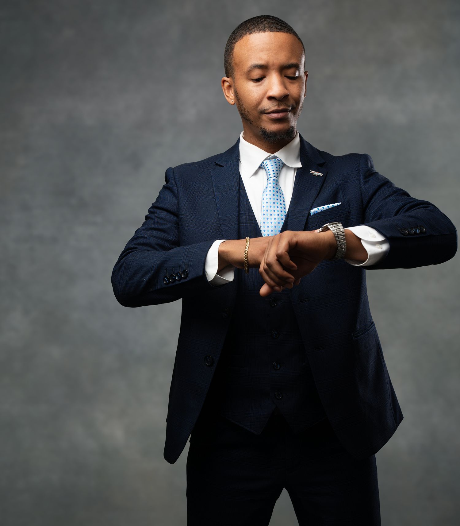 Professional in a navy suit checks his watch against a gray studio backdrop in a sequential composite image.