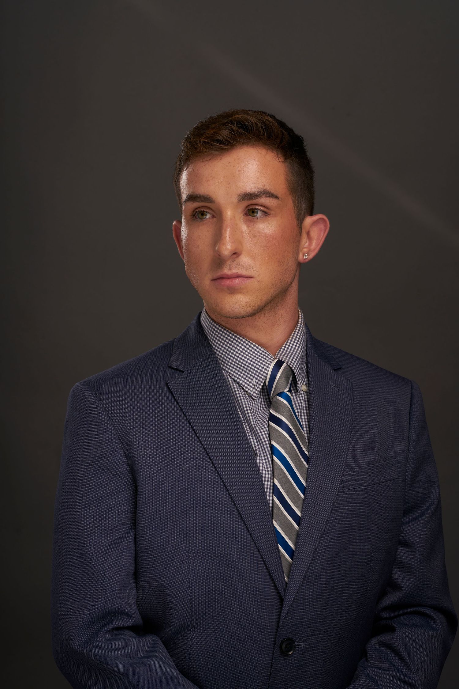 Professional portrait of person in navy pinstripe suit with striped tie against dark background.