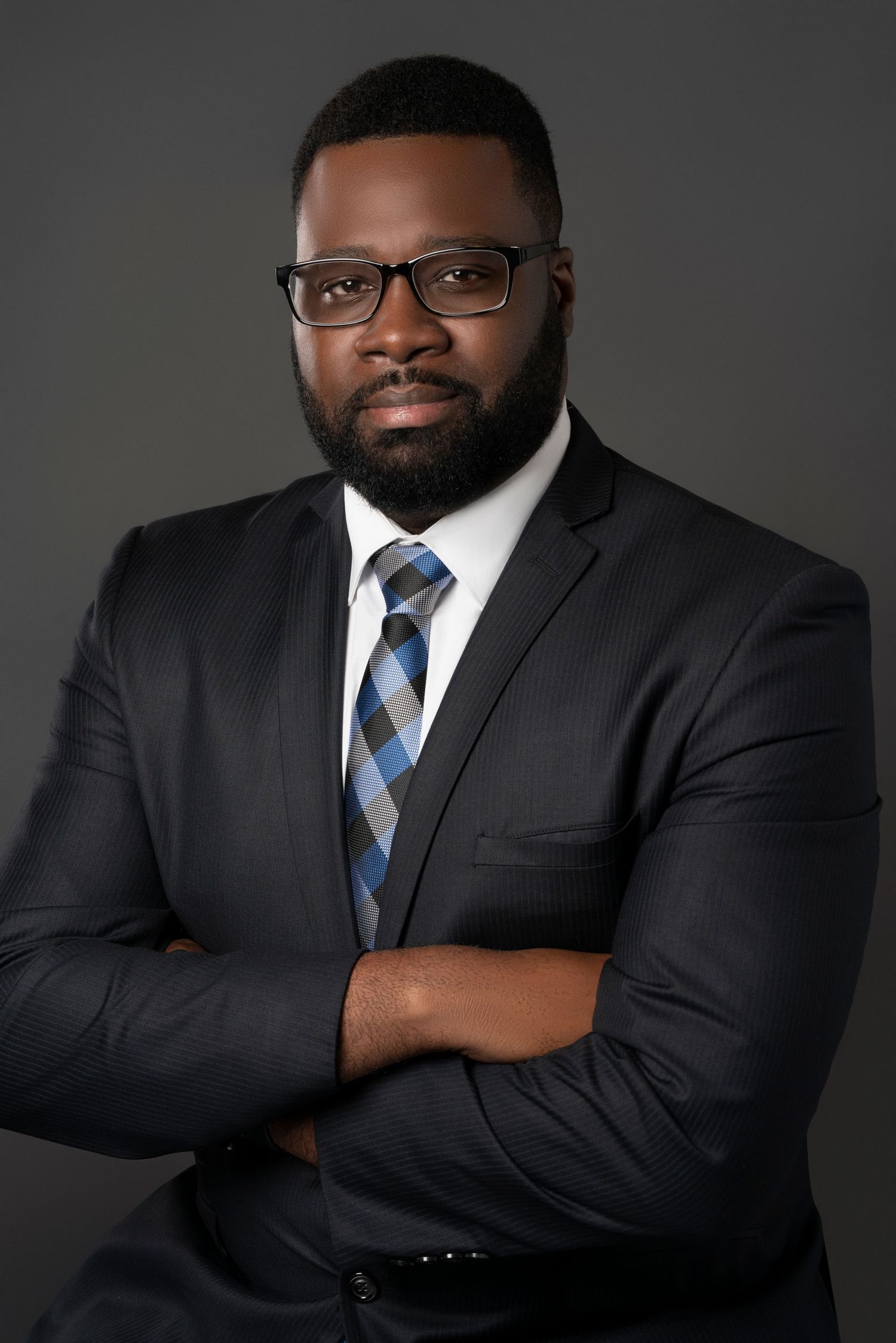 Professional headshot portraits showing a person in a dark suit and blue striped tie against a gray studio backdrop.