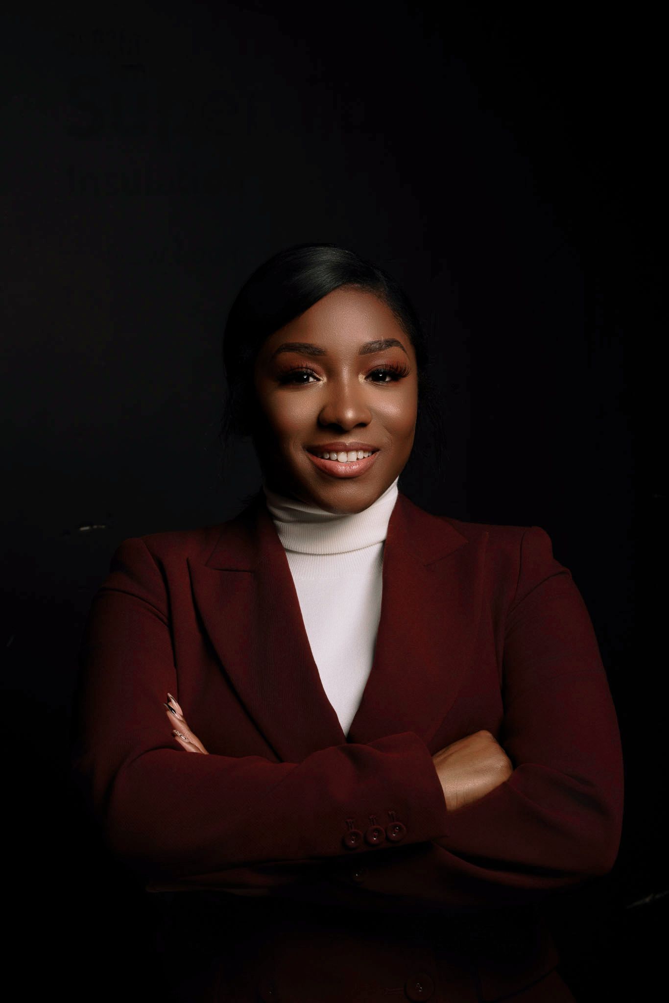 Elegant studio portraits in burgundy blazer and white turtleneck against dark background.