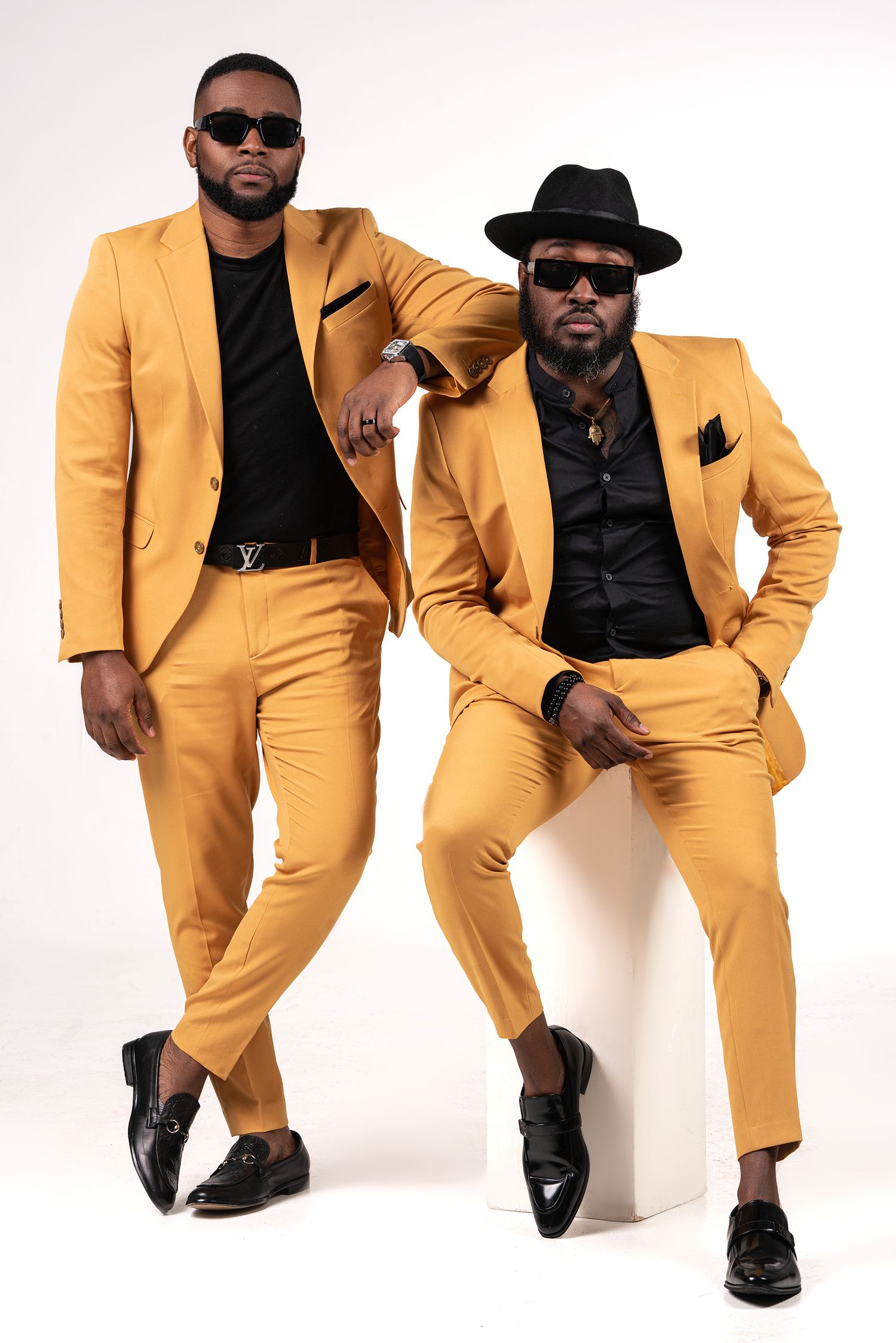 Fashion model in yellow suit and sunglasses strikes dynamic poses against white backdrop.