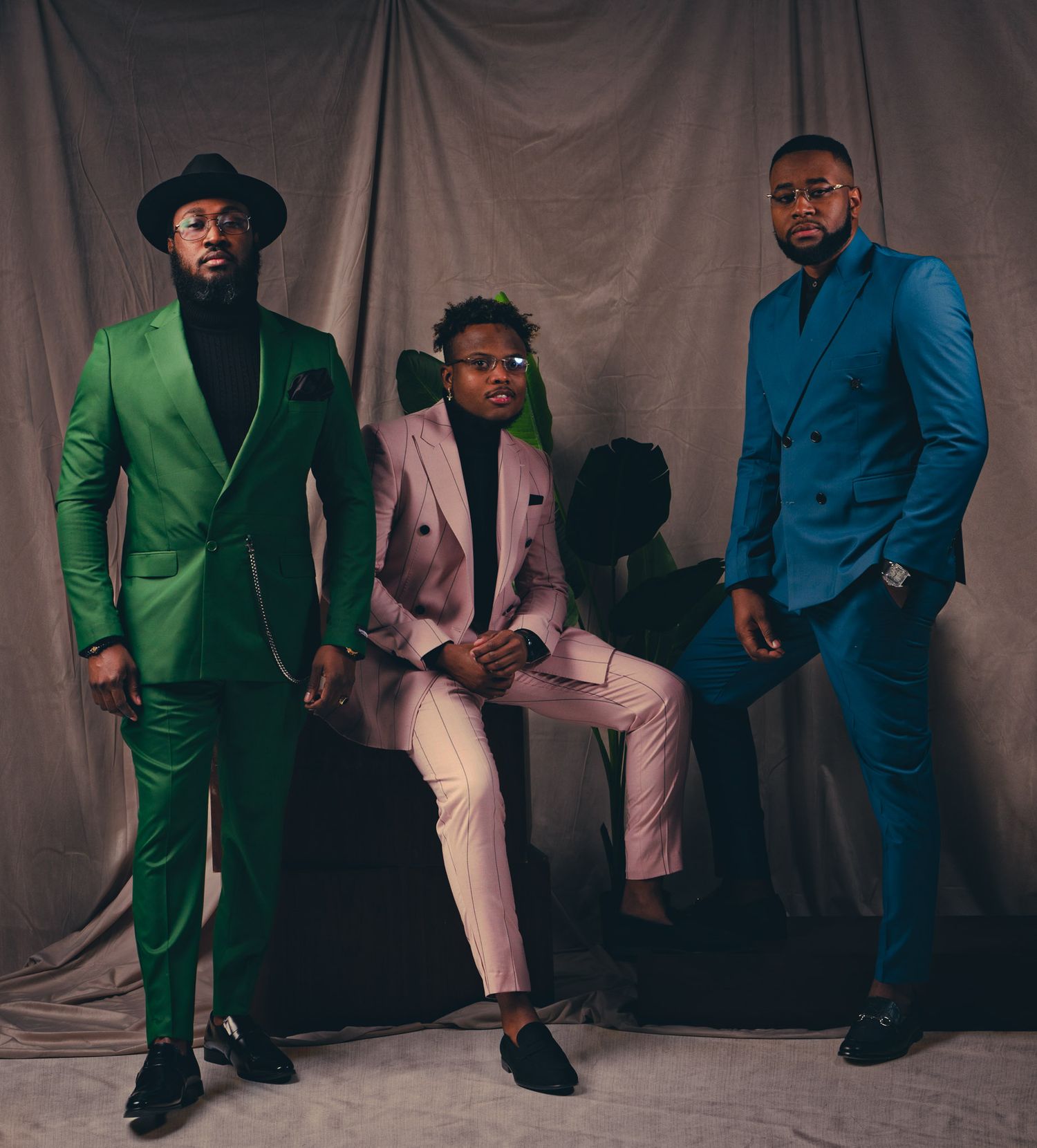 A group of men in sharp suits pose together in a studio setting with varying shades of blue and green attire.