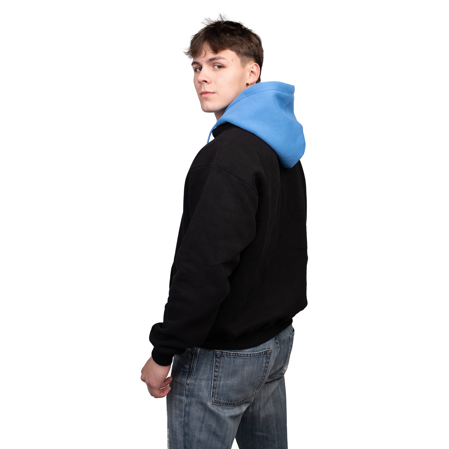 Side view of person wearing black jacket with blue hoodie and jeans against white background.