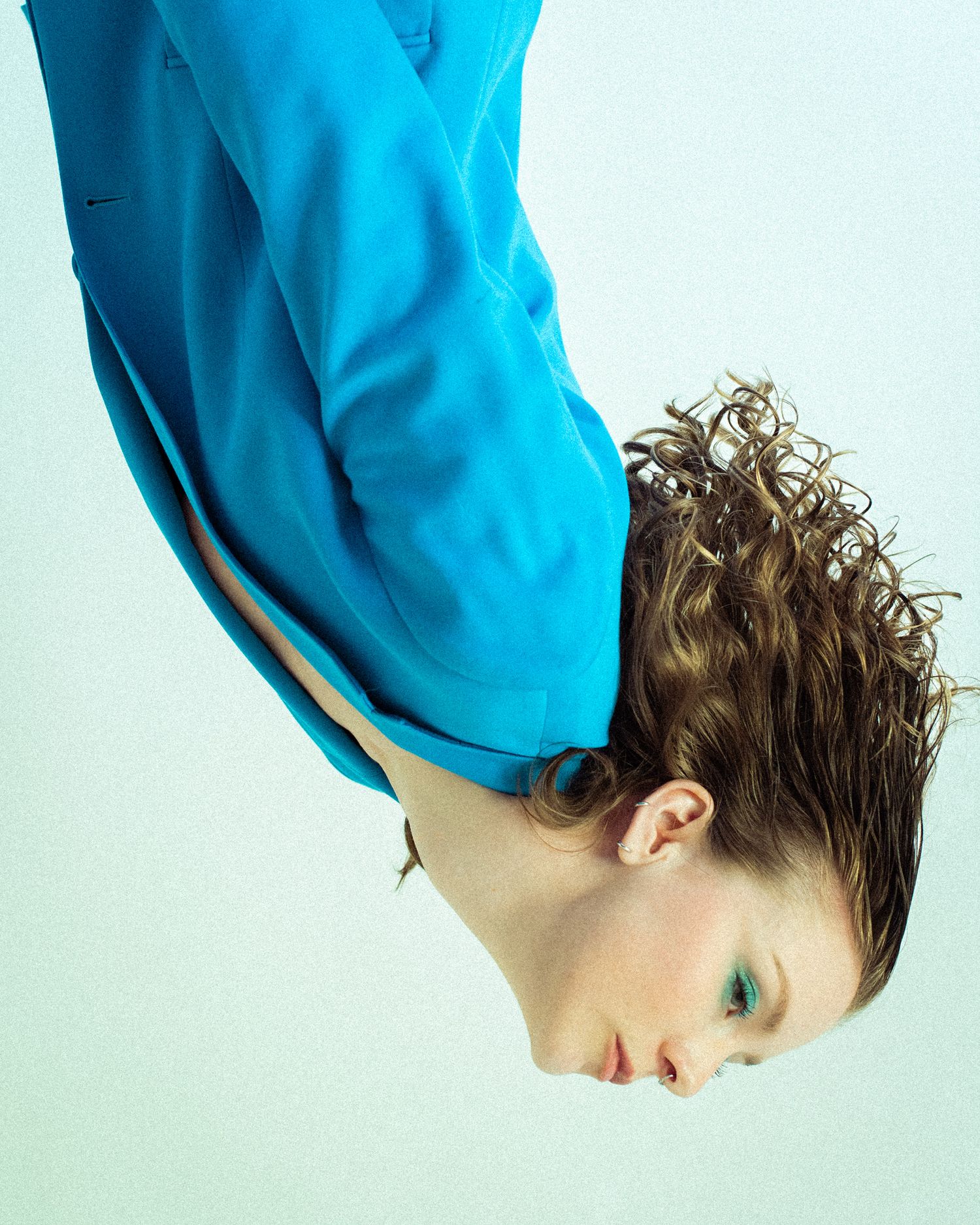 A photo of me that's inverted to look like I'm coming down from the ceiling. I am standing limp wearing a blue blazer with blue eye makeup.