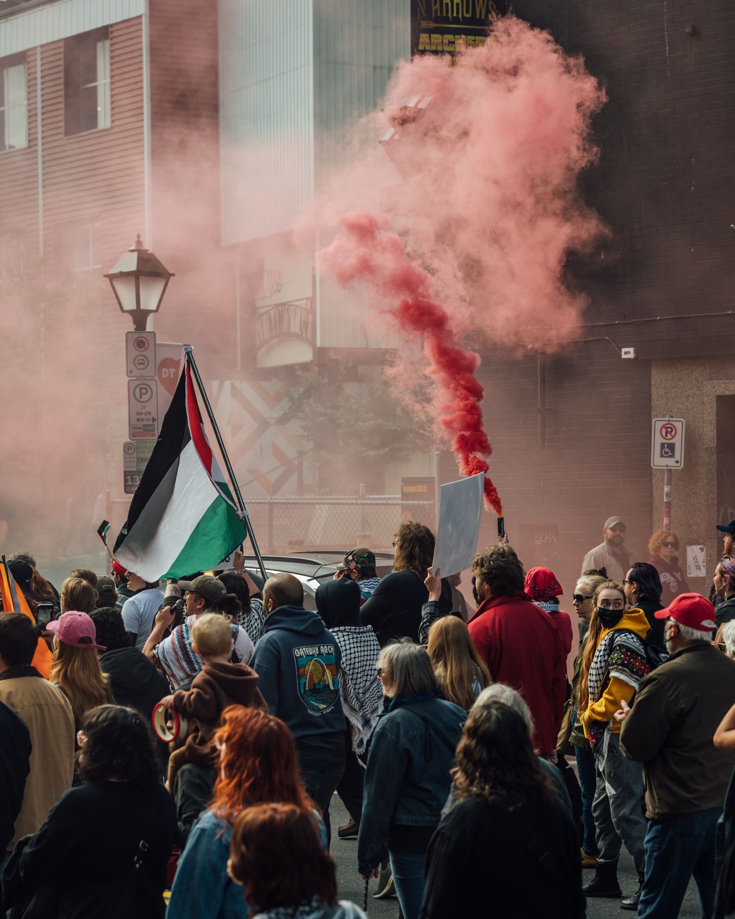 Coloured smoke and flags are visible above a crowd of protesters marching down a street.