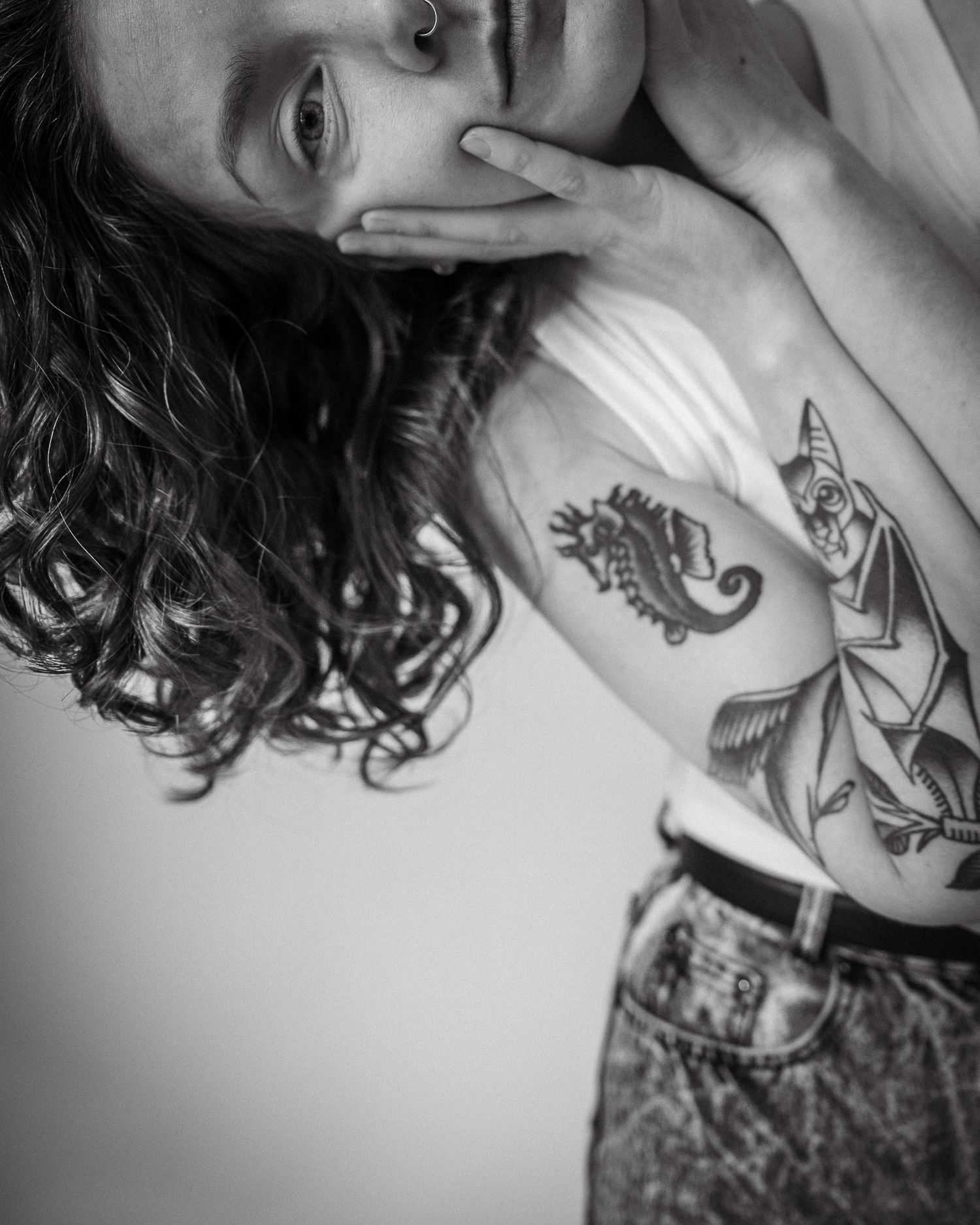A black and white photo of Tania Heath, they are 1/4th in frame and twisted down. You can only see half of the face. They have tattoos.