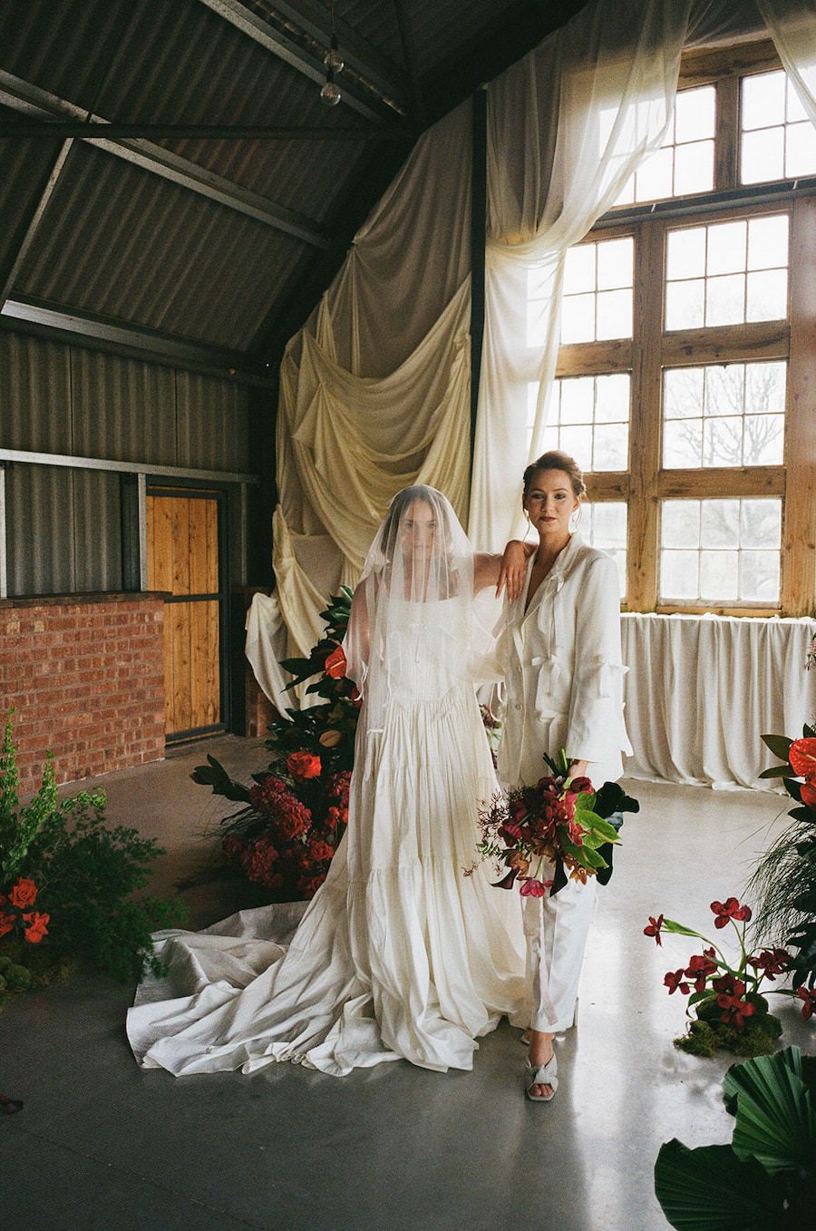 Same sex couple pose for couples at The Giraffe Shed wedding venue in Newtown, Wales. Image is on 35mm Film. Red Flowers decorate the room.