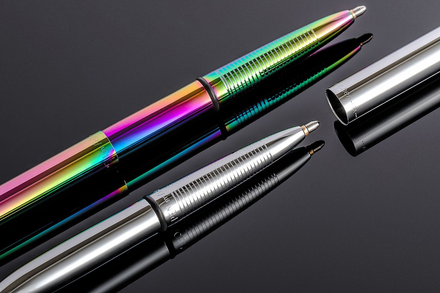 Three sleek metal pens lined up showing iridescent rainbow and silver finishes with ribbed textures.