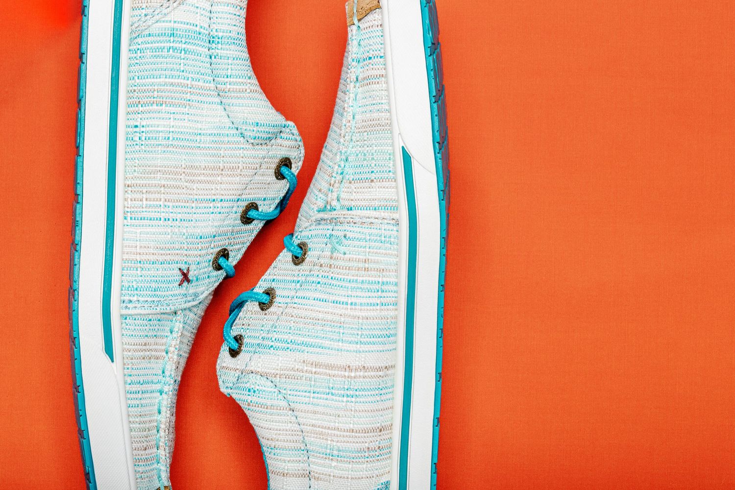 White and teal sneakers arranged in a row against a bright orange background for product photography.