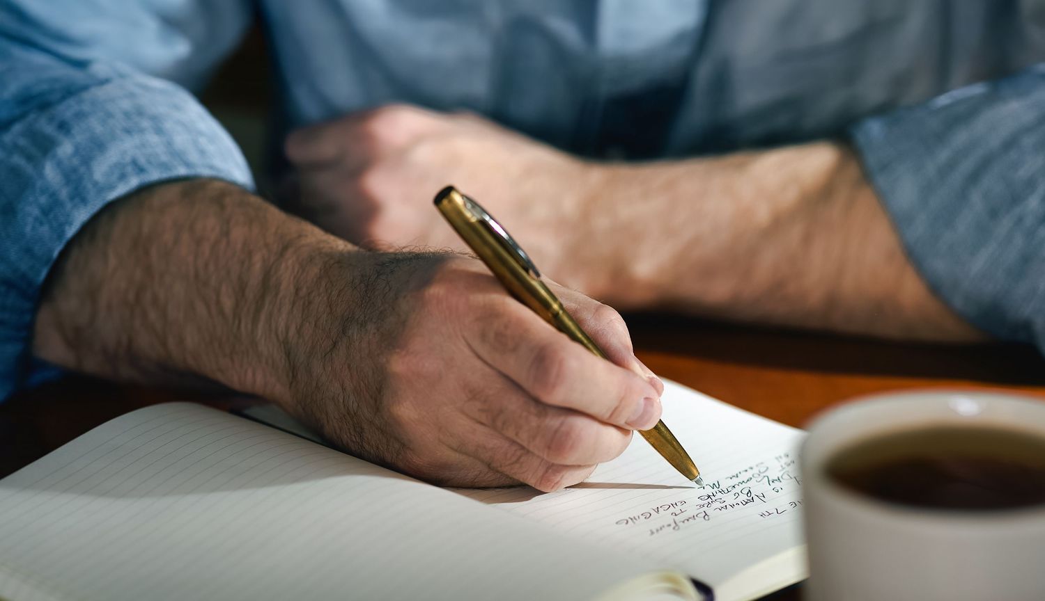 A person's hands write with a pen on paper in a close-up view.