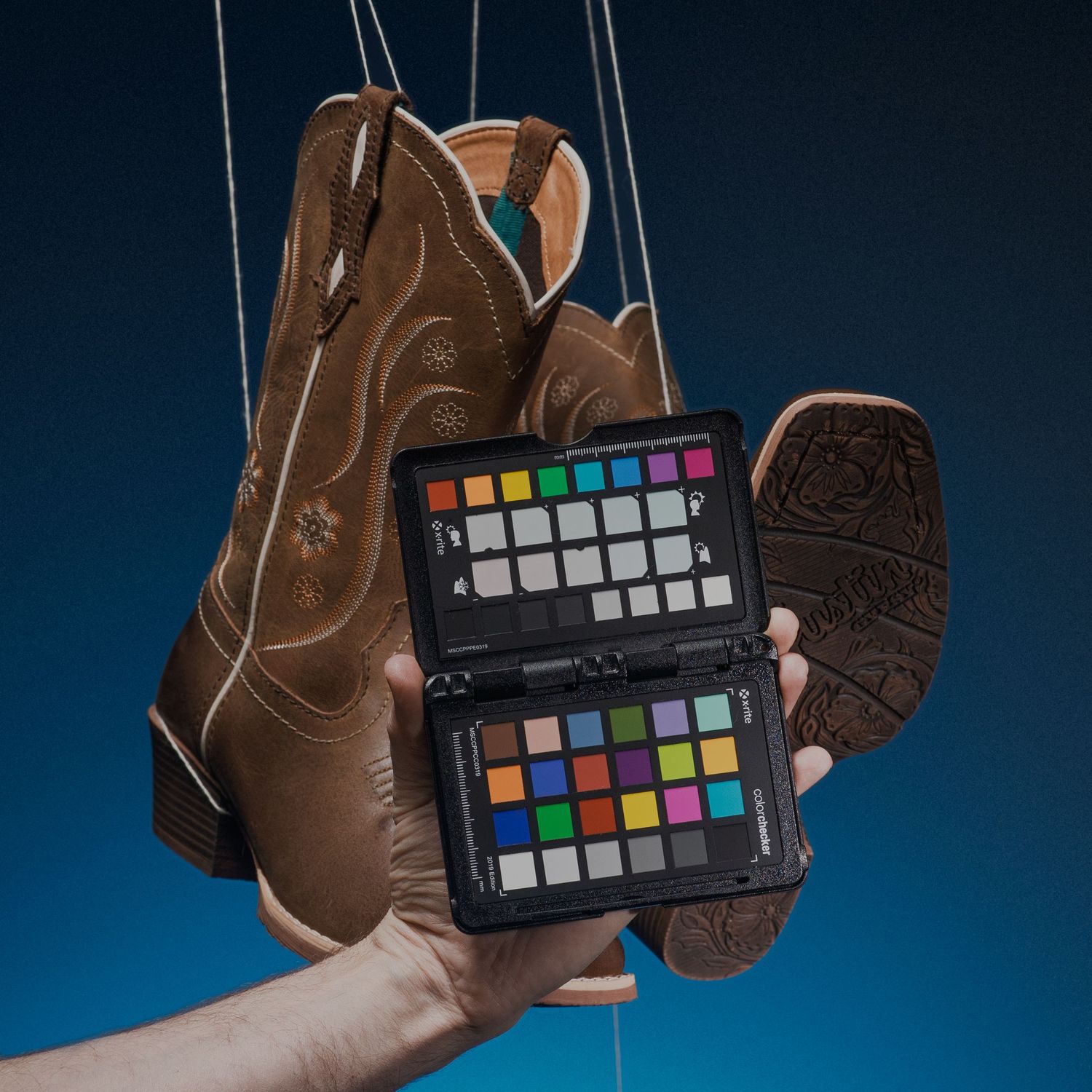 Brown cowboy boots displayed with color calibration card against dark background.