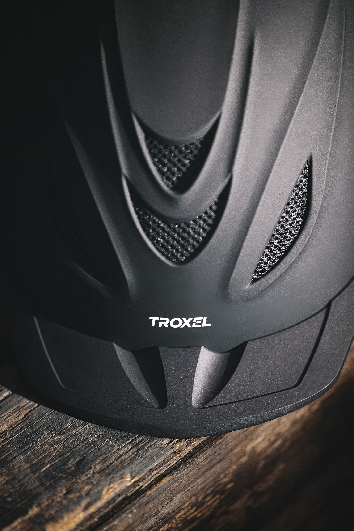 Close-up detail of a black Troxel safety helmet on wooden surface. Product Photography