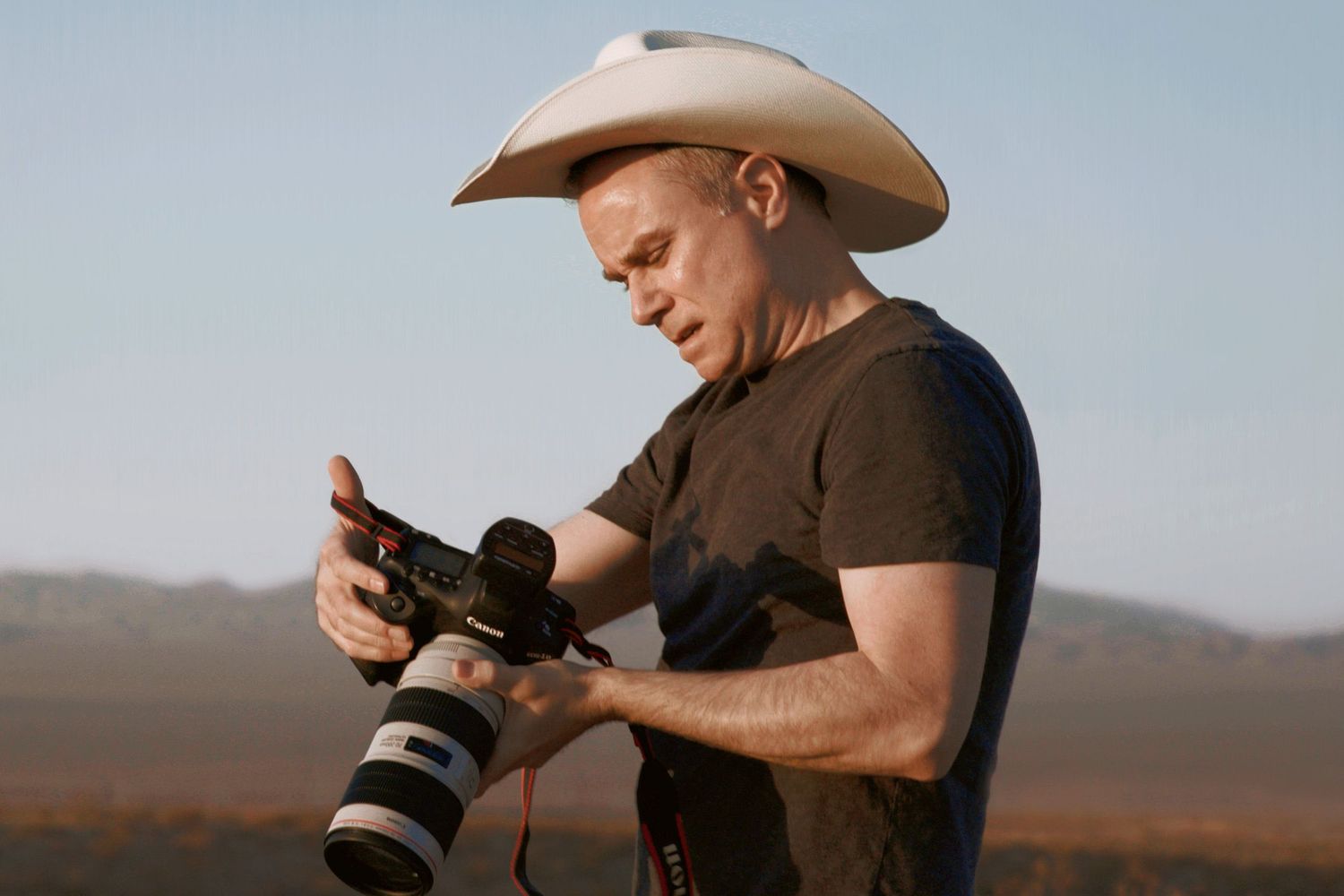 Photographer with camera and cowboy hat working in desert setting.