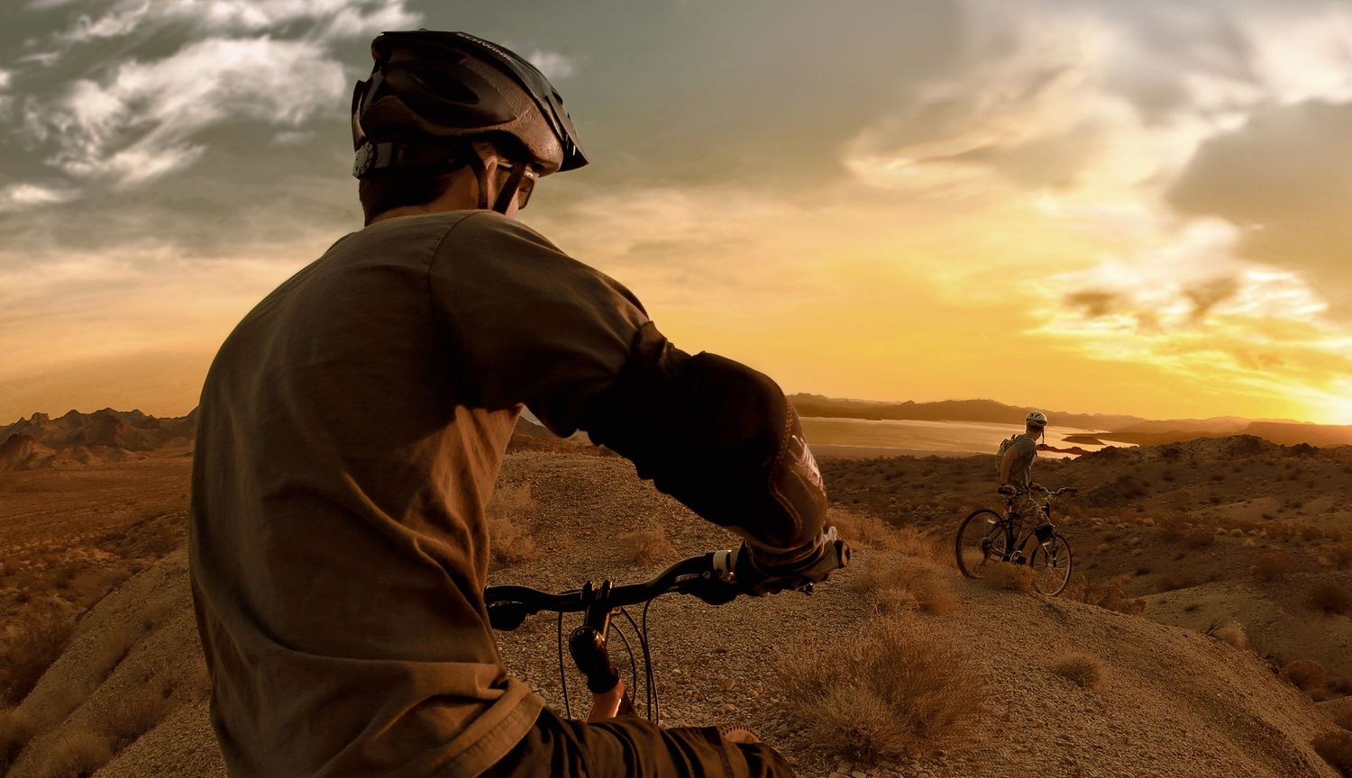 Mountain bikers silhouetted against golden sunrise over desert terrain. Editorial lifestyle photography for Fisher Space Pen Company.