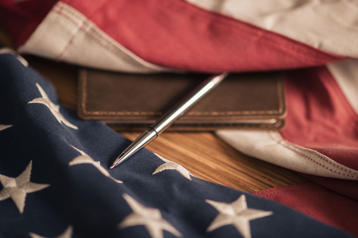 Close-up detail of an American flag with stars and stripes, a leather journal, and a Fisher Space Pen Chrome Bullet Pen.