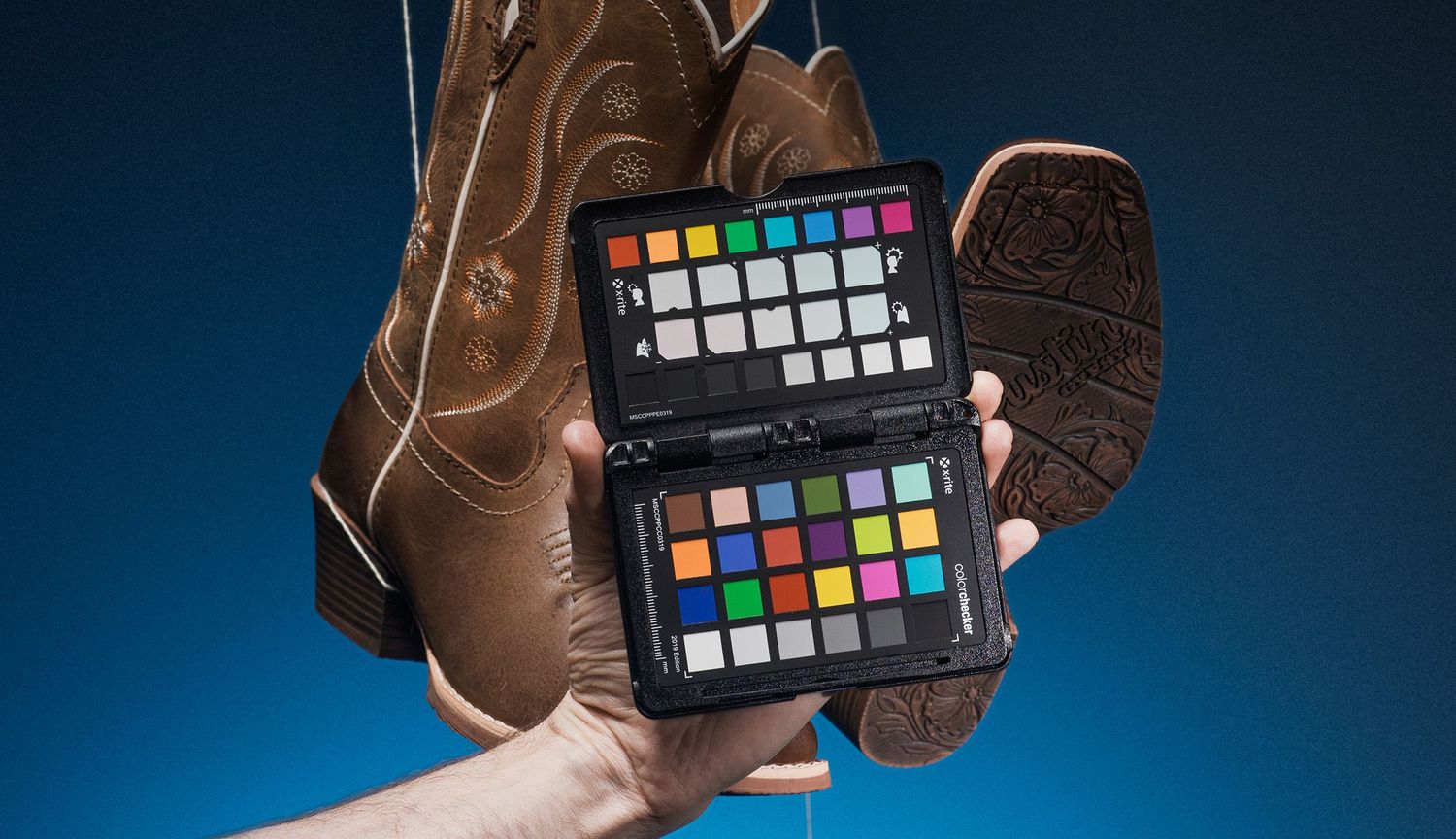 A color calibration card is held against a brown leather boot against a blue background lighting setup.