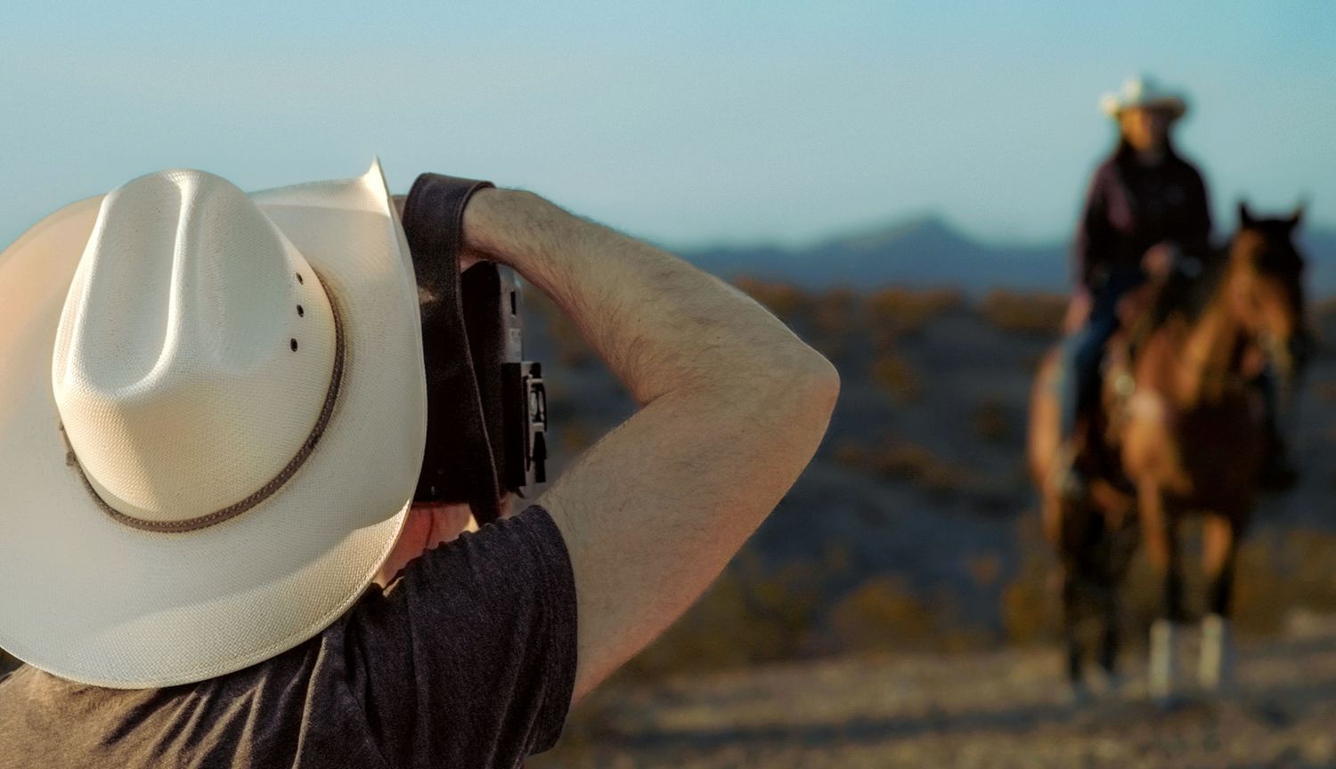 Horseback riders silhouetted against desert horizon during photo shoot.