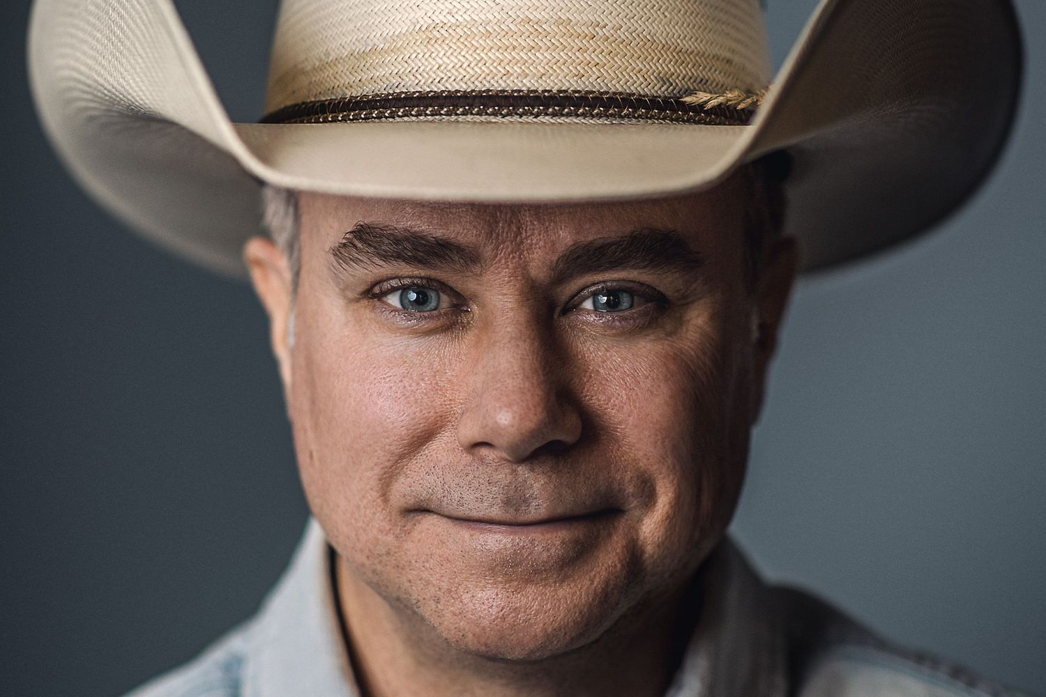Person wearing cowboy hat in professional headshot against gray studio background.