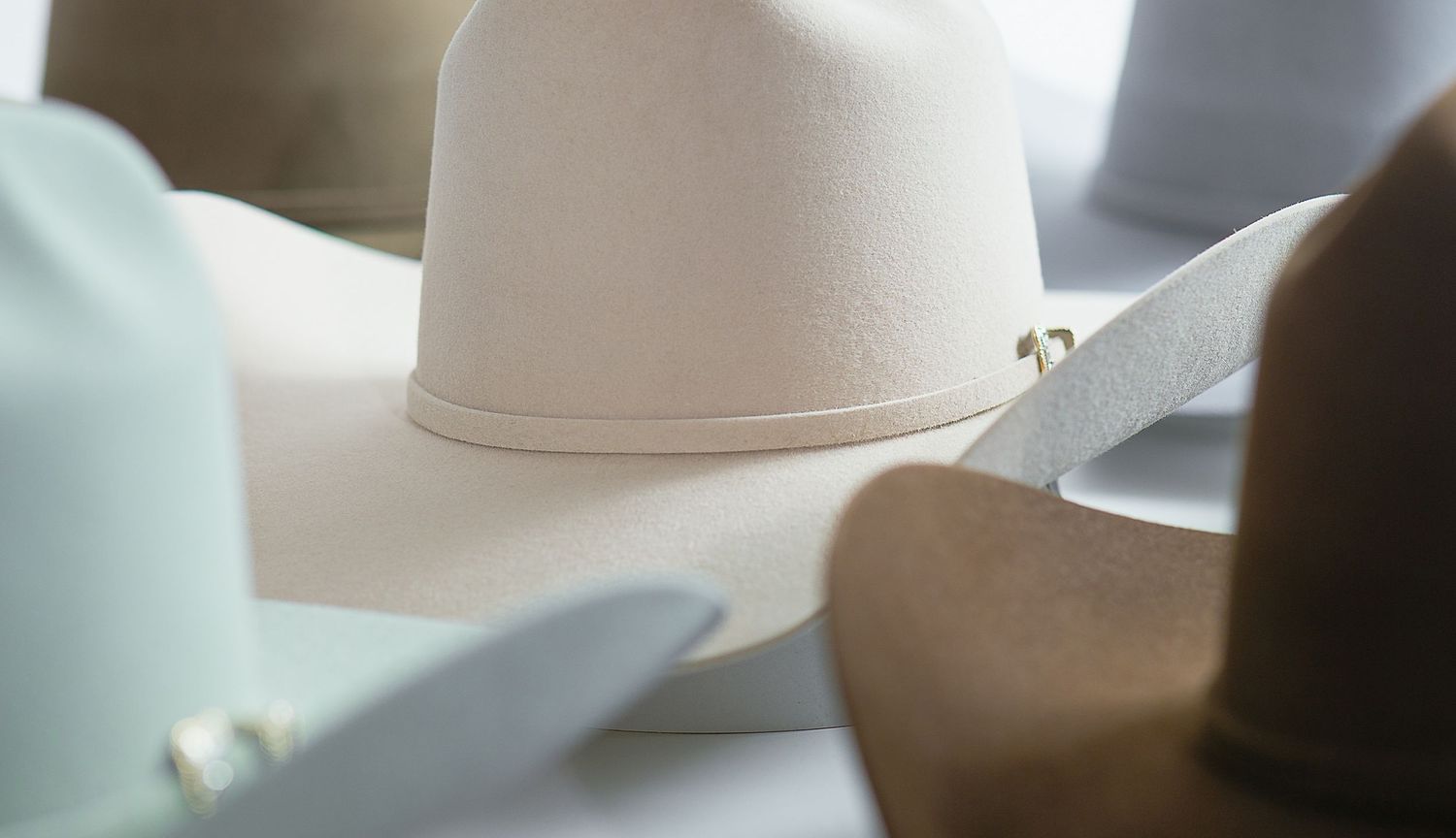 Several colored Master Hatters of Texas cowboy hats sit in a row on a light colored surface in natural lighting. Product photography
