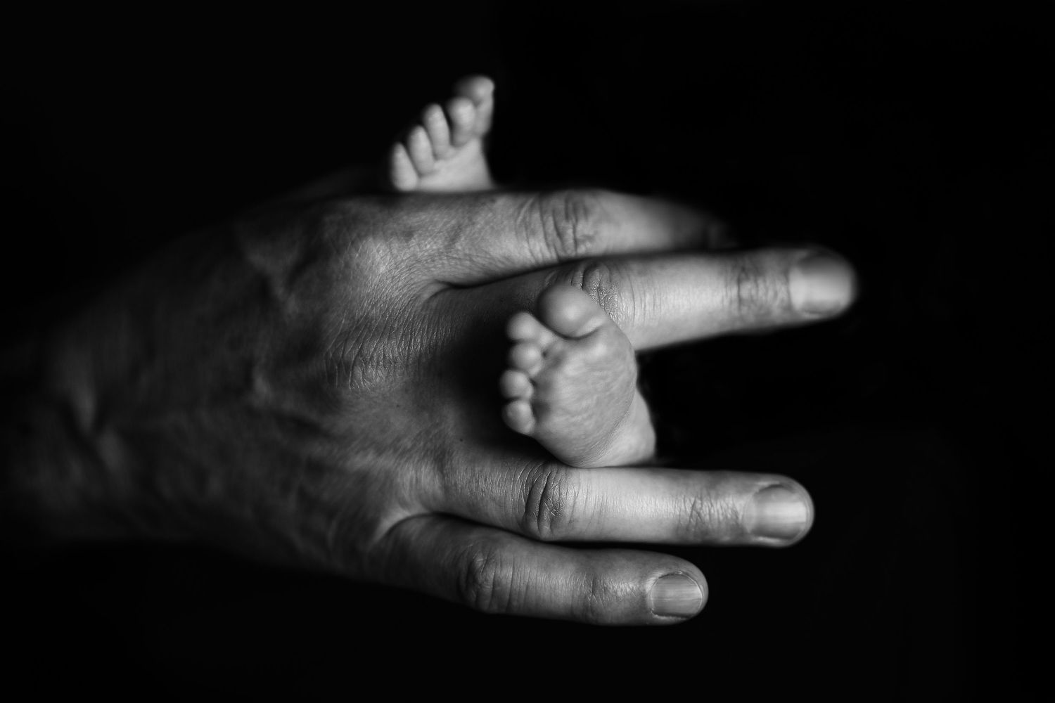 Dramatic black and white photo of hand and baby feet.  Hatched Newborn and Family Photography. Madison, Monona, Verona, Mount Horeb, WI