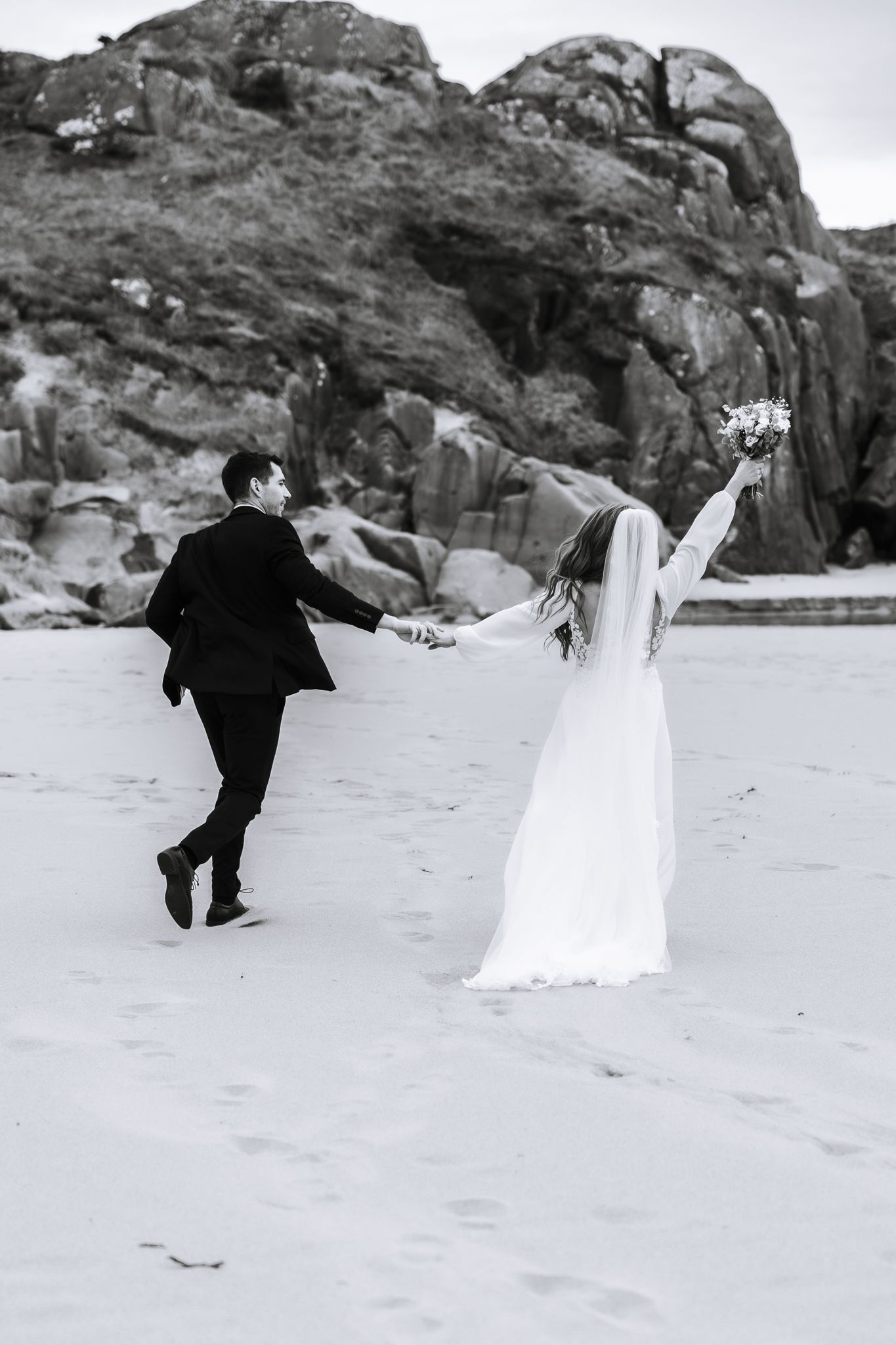Brudgom og brud som springer på stranden på Sandvedsanden