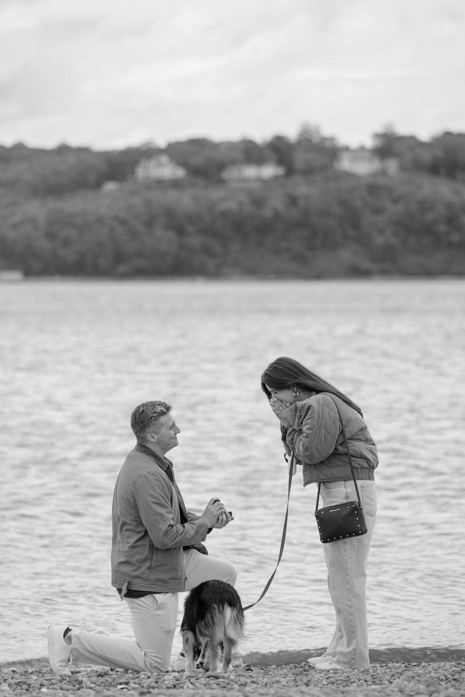 Two people fishing by a lake with their dog on an overcast day.