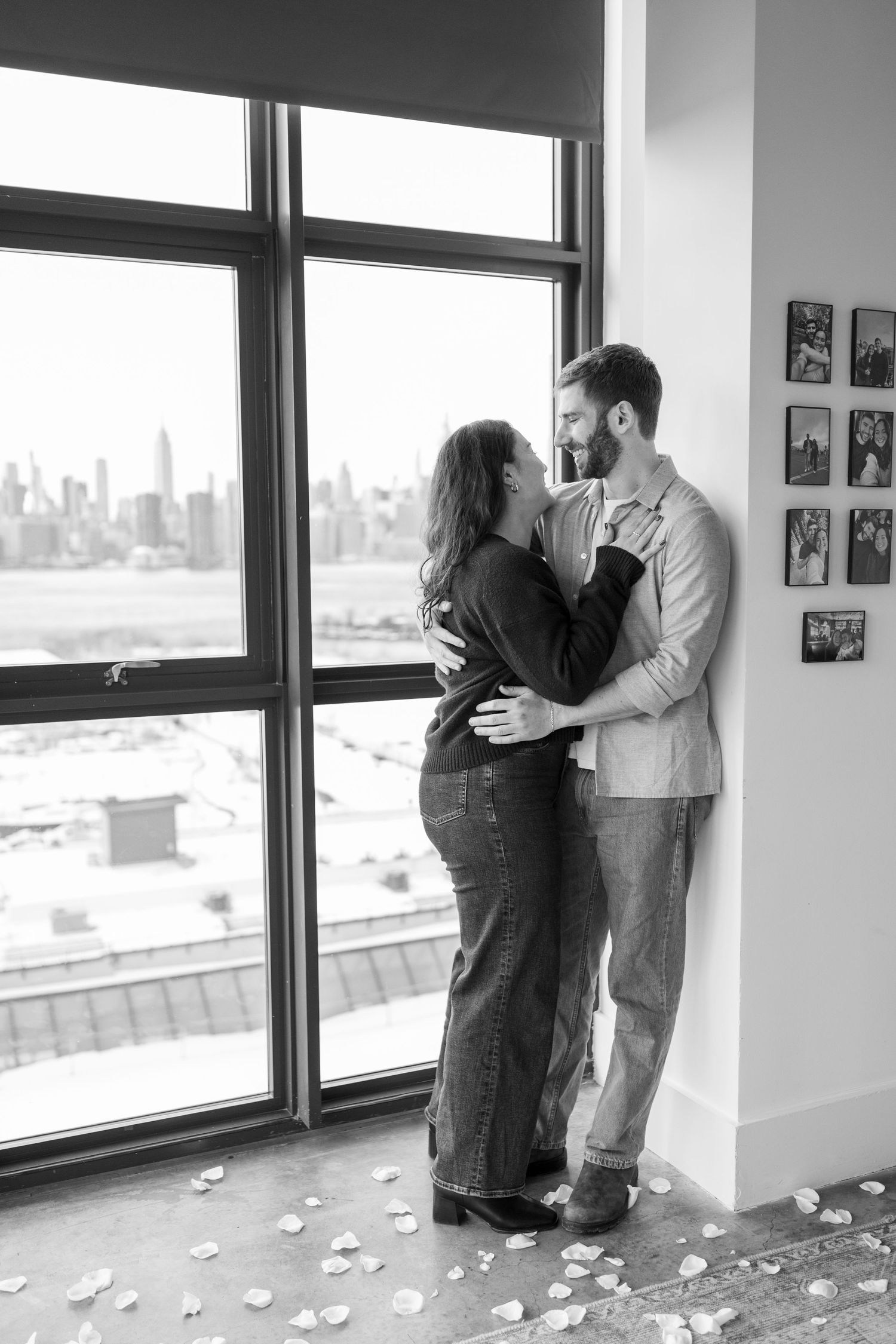 A romantic black and white sequence of three photos showing a couple embracing near large windows with a city view.