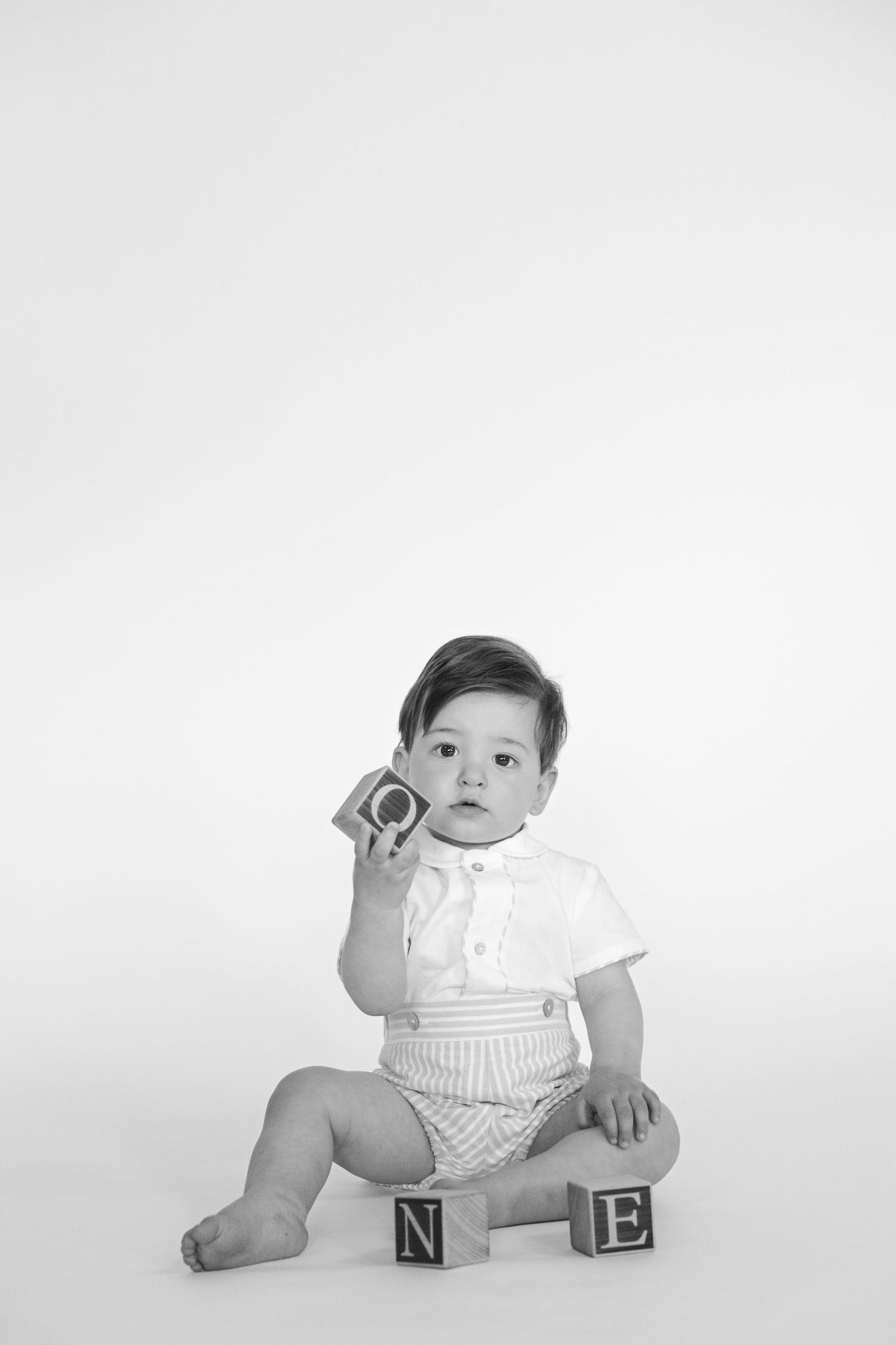Baby in white outfit poses with alphabet blocks in black and white photo.