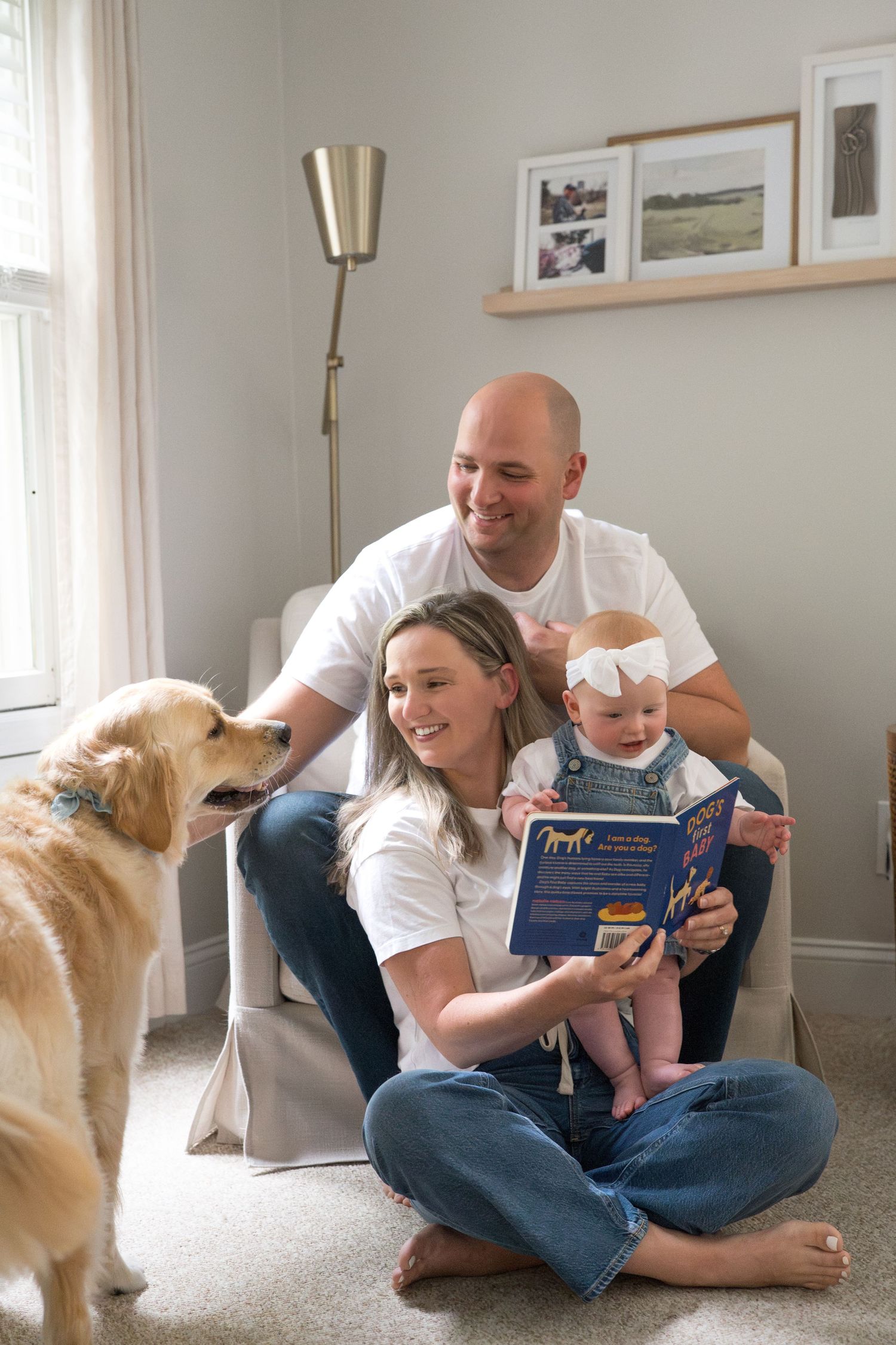 Family relaxing on carpet at home with their golden retriever while reading a book together.