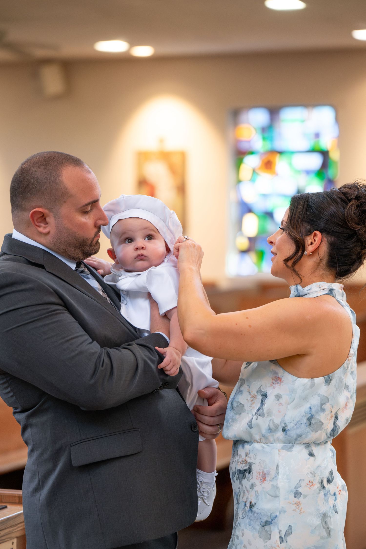 Baby in white christening gown being held during baptism ceremony in church.