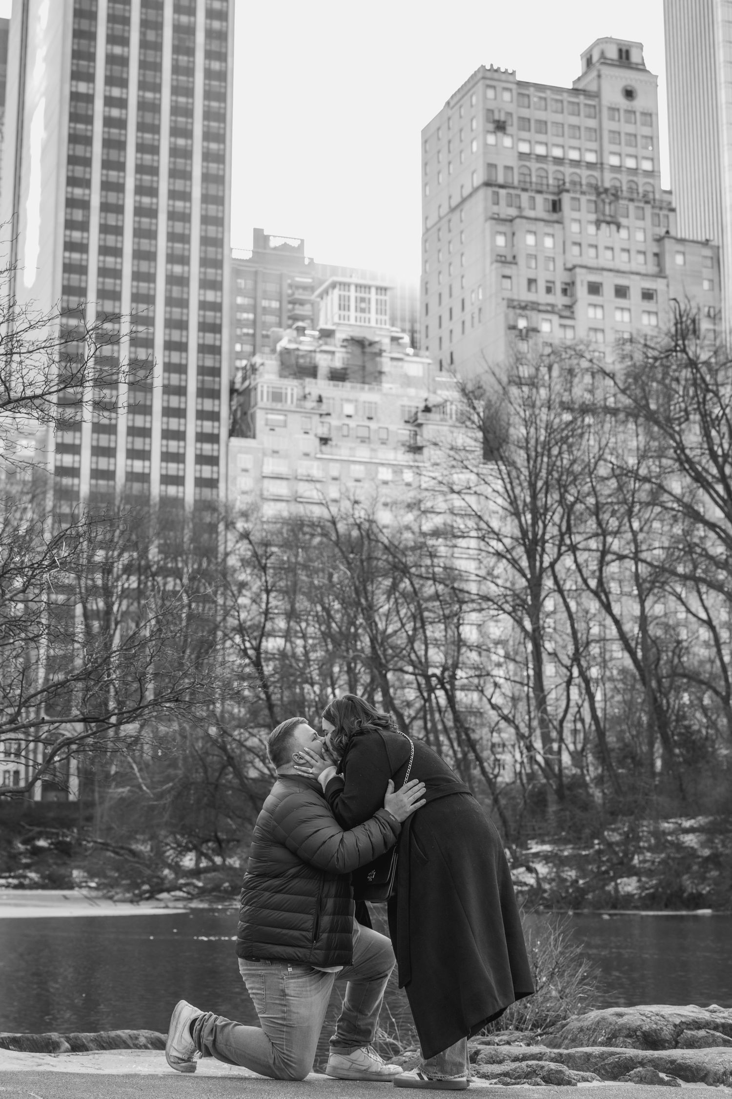 A romantic winter scene in Central Park with the NYC skyline visible through bare trees.
