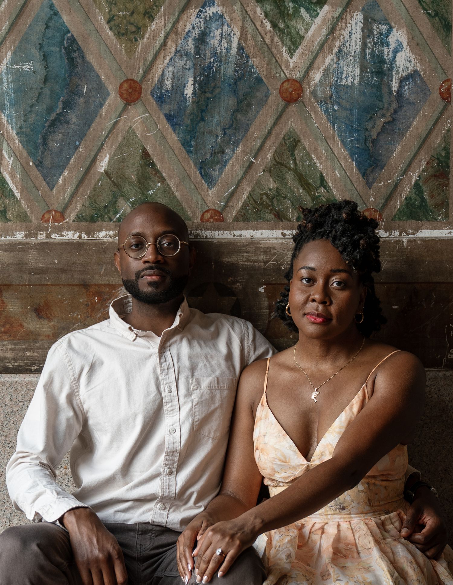 A romantic couple in white outfits sits close together against a rustic blue wall with a vintage weathered texture.