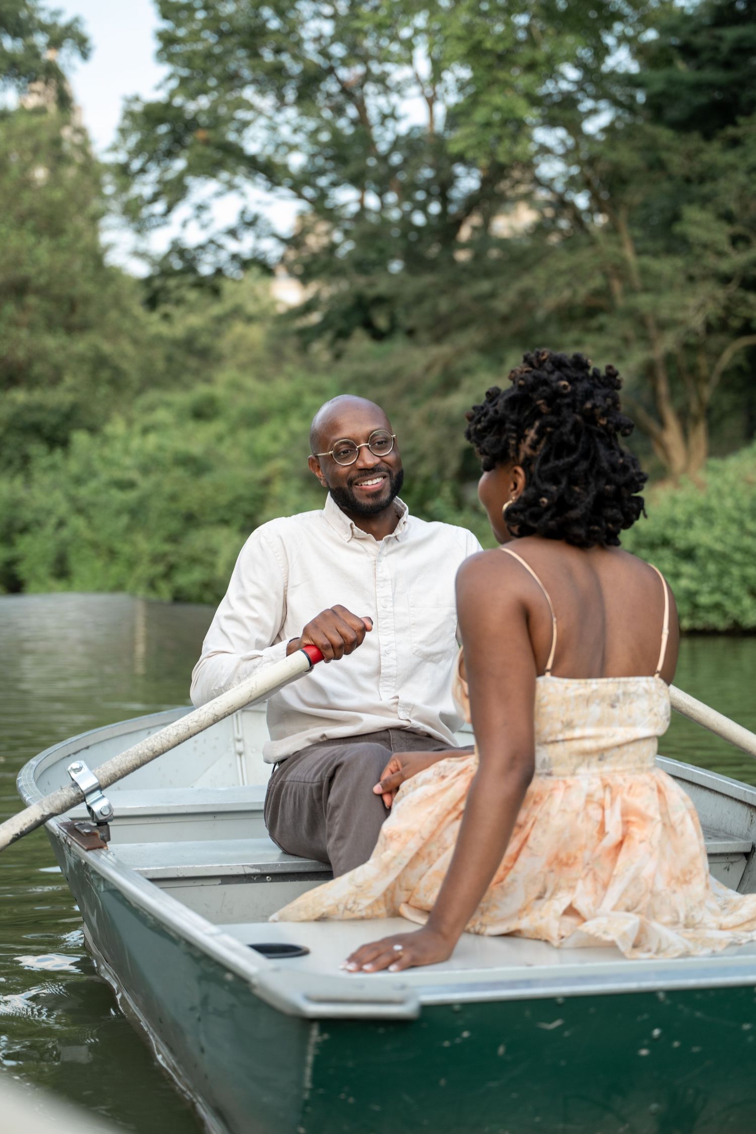 A couple shares romantic moments while sitting in a rowboat on a peaceful lake.