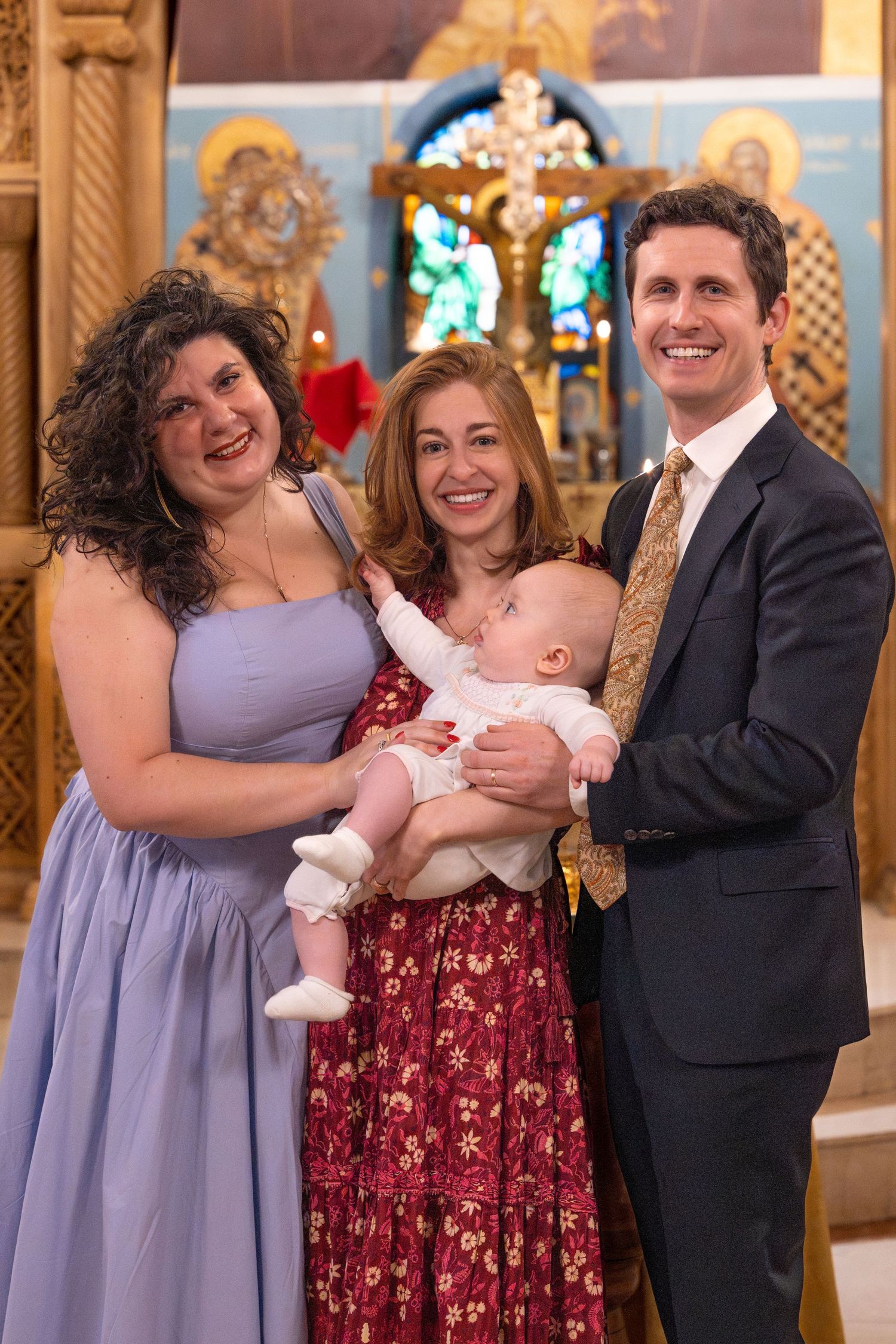 A baby's baptism celebration in a church with family members posing in front of religious icons and stained glass.