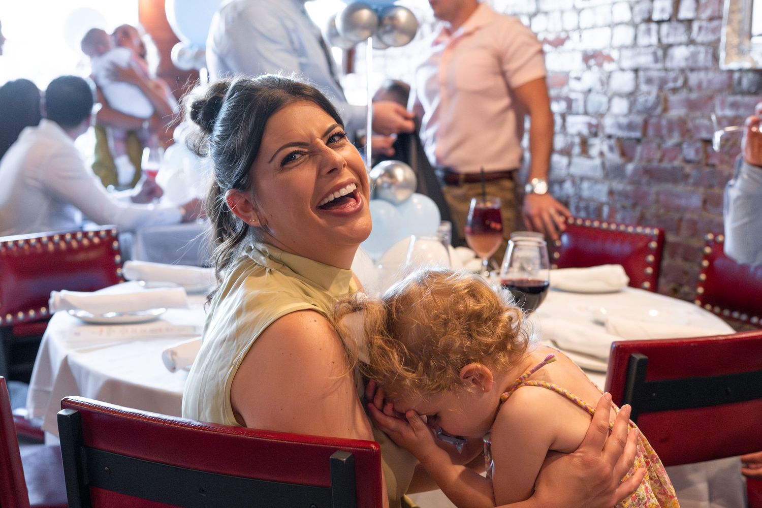 People enjoying a lively celebration at a restaurant with red booth seating and exposed brick walls.