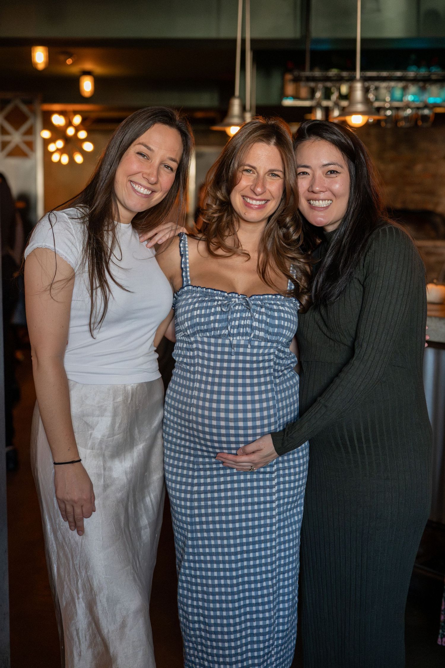 Three friends in casual attire posing together against a dimly lit restaurant backdrop.