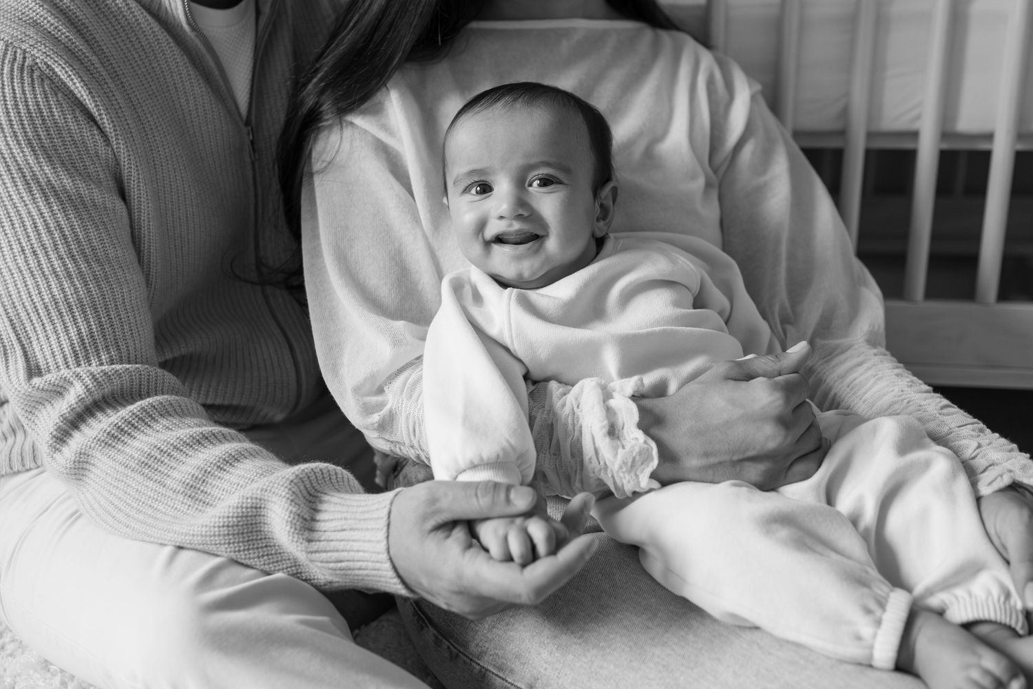 Black and white photo of a smiling baby being held by a parent, sitting contentedly in loving arms.